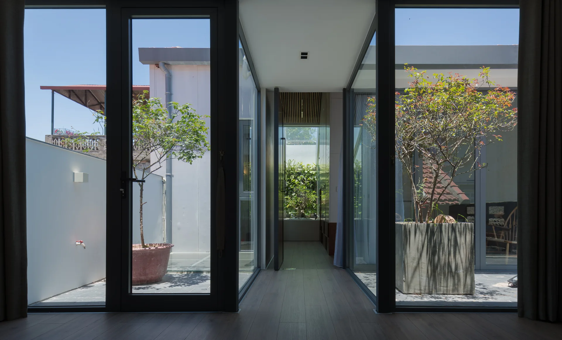 A modern interior hallway features floor-to-ceiling glass walls looking out onto small enclosed courtyards with potted plants.
