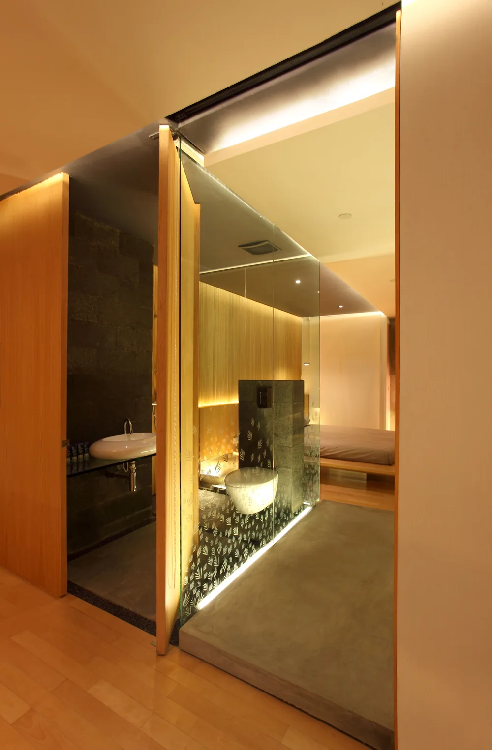 A modern bathroom features a glass partition with etched details, a wall-mounted toilet, and warm wood wall paneling.