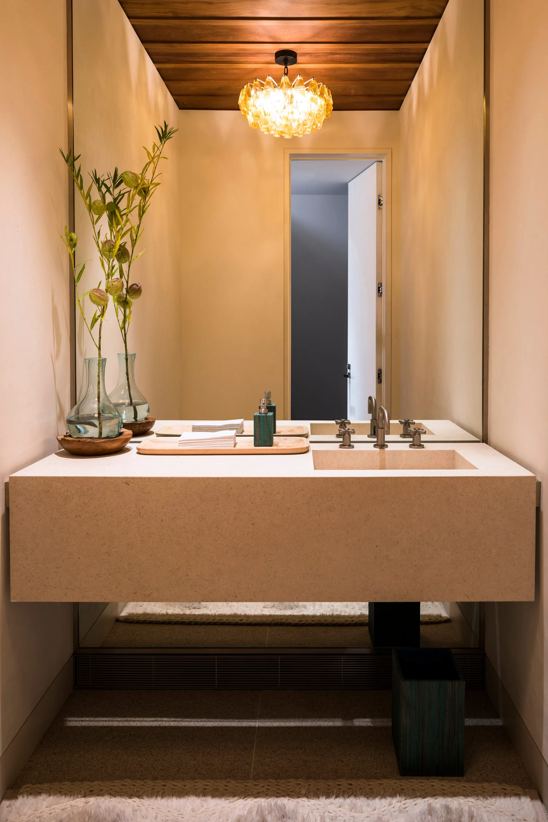 A minimalist powder room features a thick floating stone vanity with an integrated sink, a large wall mirror, and a warm wood plank ceiling.