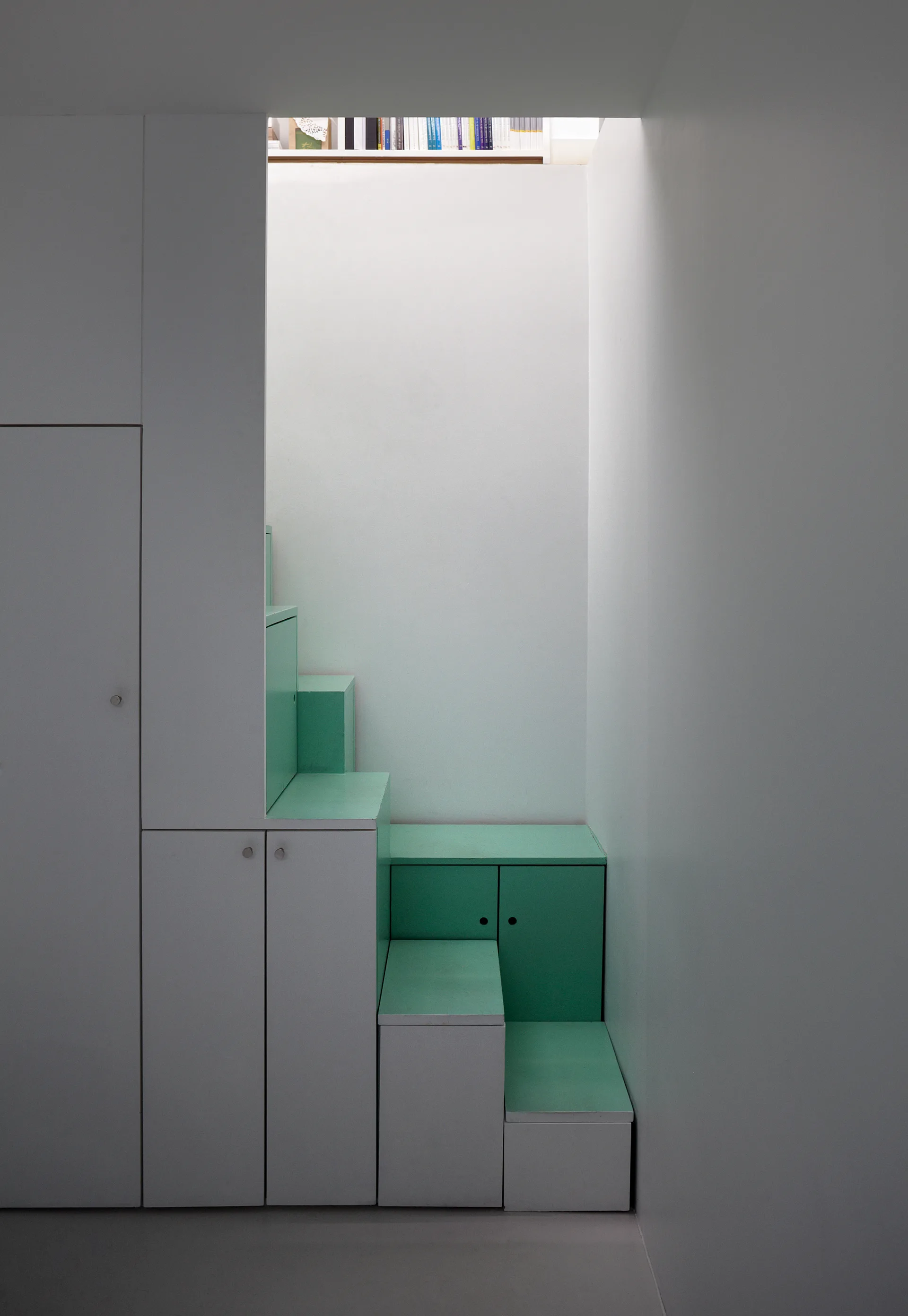 A modern minimalist staircase with alternating white and mint green steps that double as integrated storage cabinets.