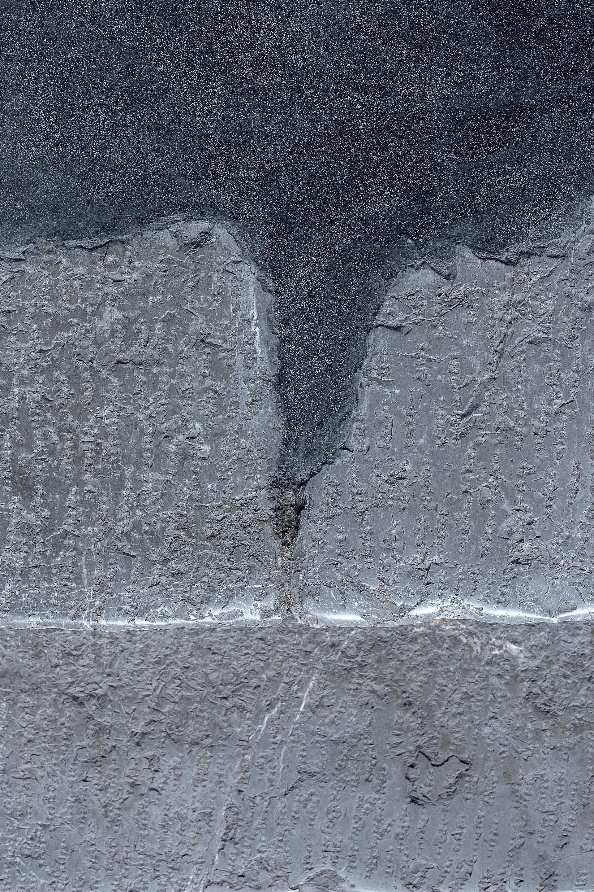 A close-up of textured gray stone wall cladding featuring a rough split-face surface and a dark granulated grout joint.