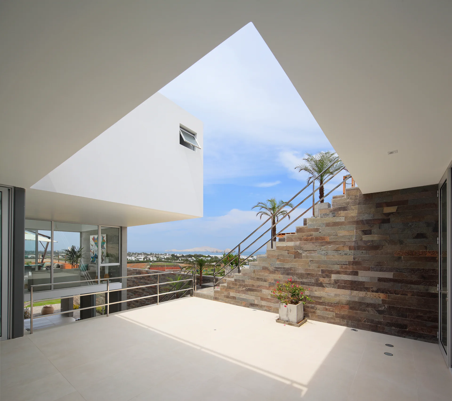 An open-air modern terrace featuring a white geometric roof overhang with a large triangular cutout, a stone clad staircase, and metal railings.
