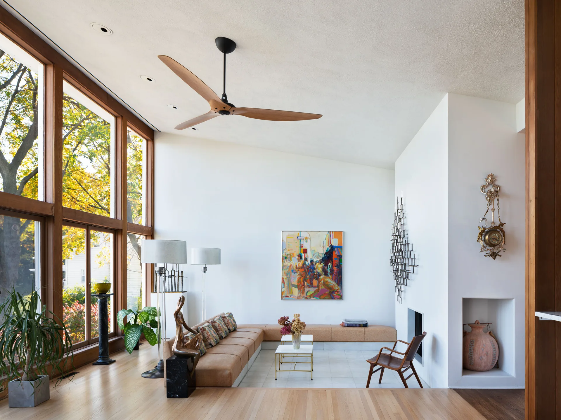 A sunken mid-century modern living room features a tan sectional sofa, large wood-framed windows, and a white fireplace.