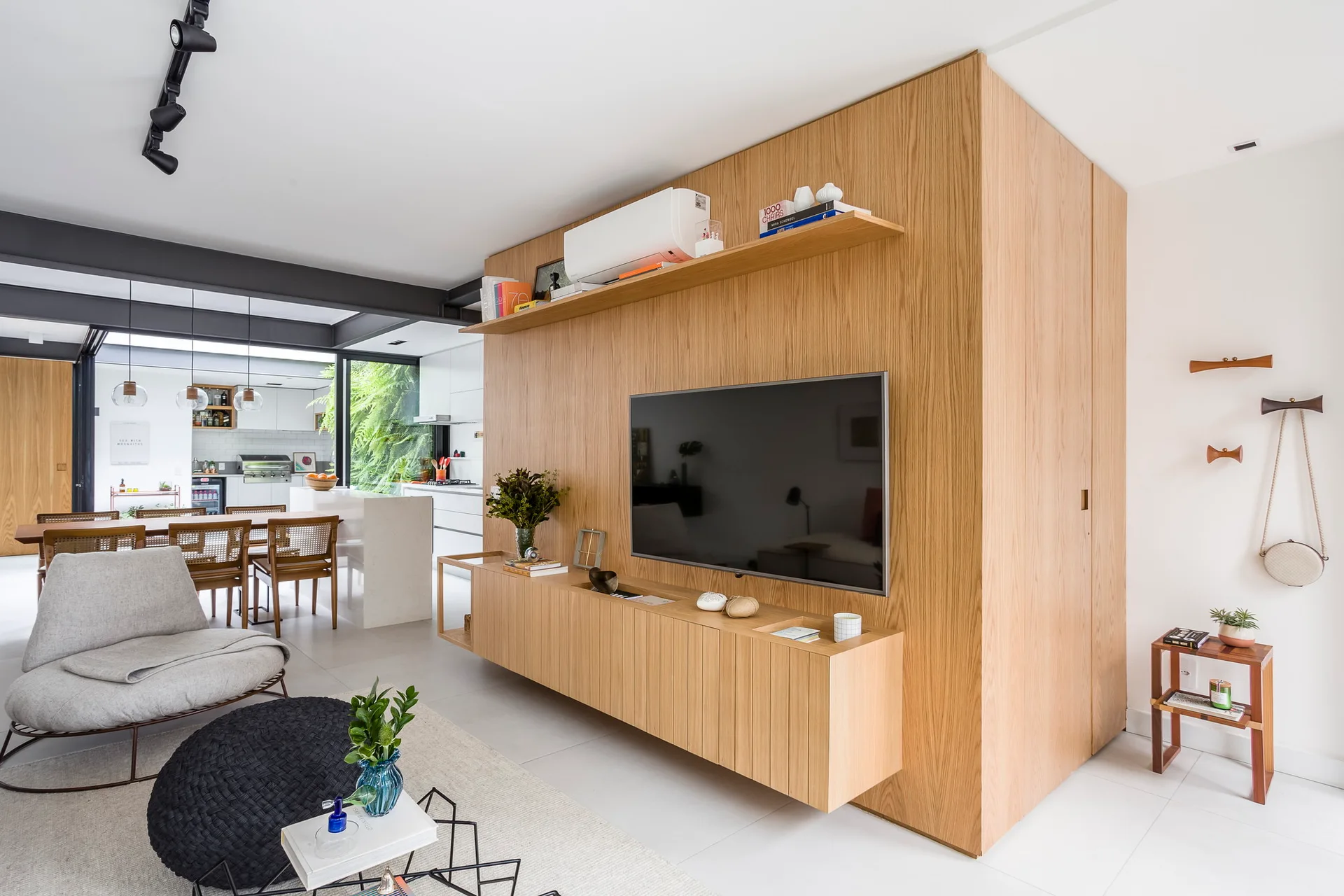 A contemporary living room featuring a large wood-paneled media wall with a mounted TV, a grey lounge chair, and dark metal ceiling beams.