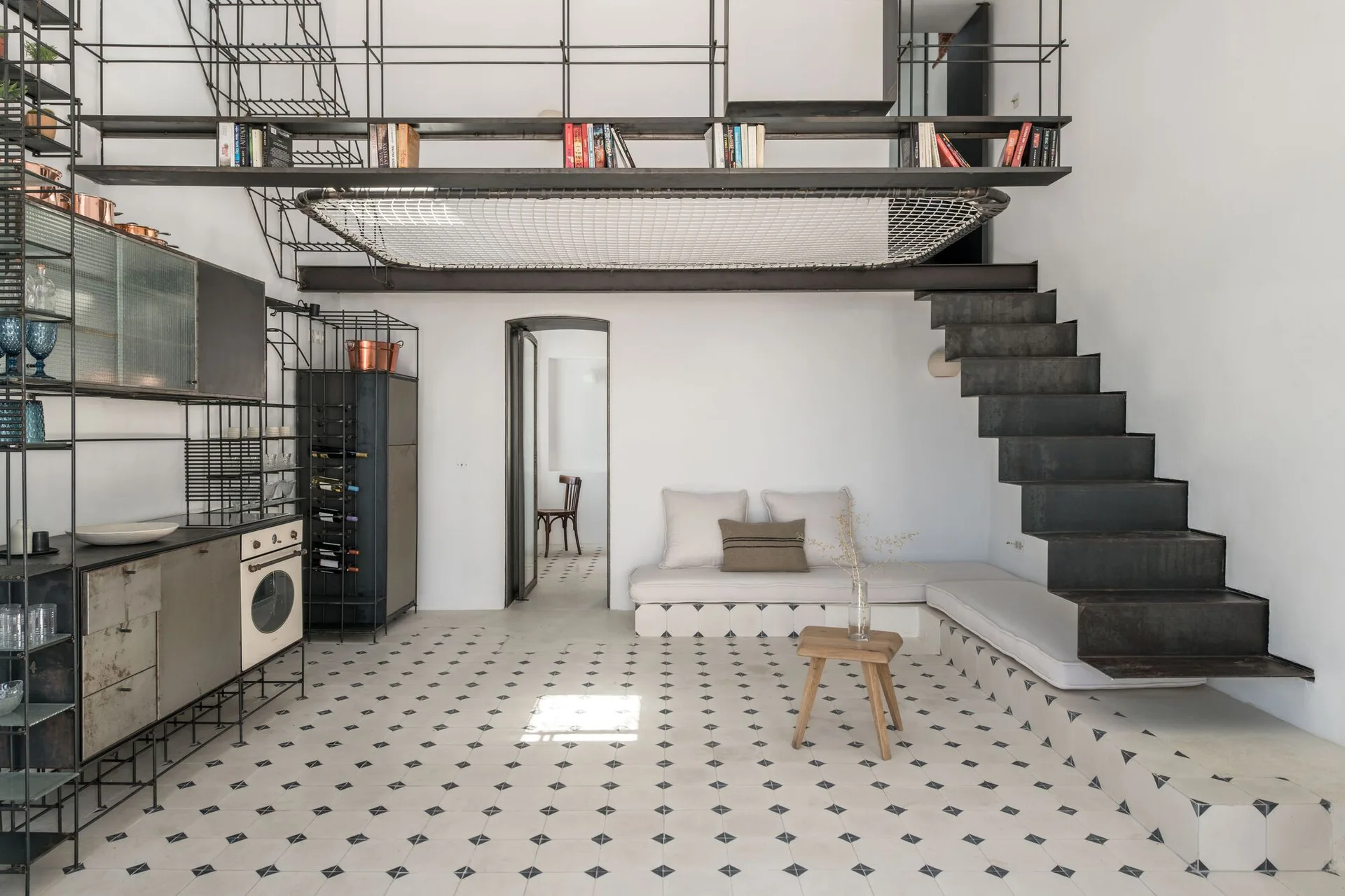 An industrial loft living room with a black metal staircase, a built-in tiled sofa, and a suspended mesh net on the mezzanine level.
