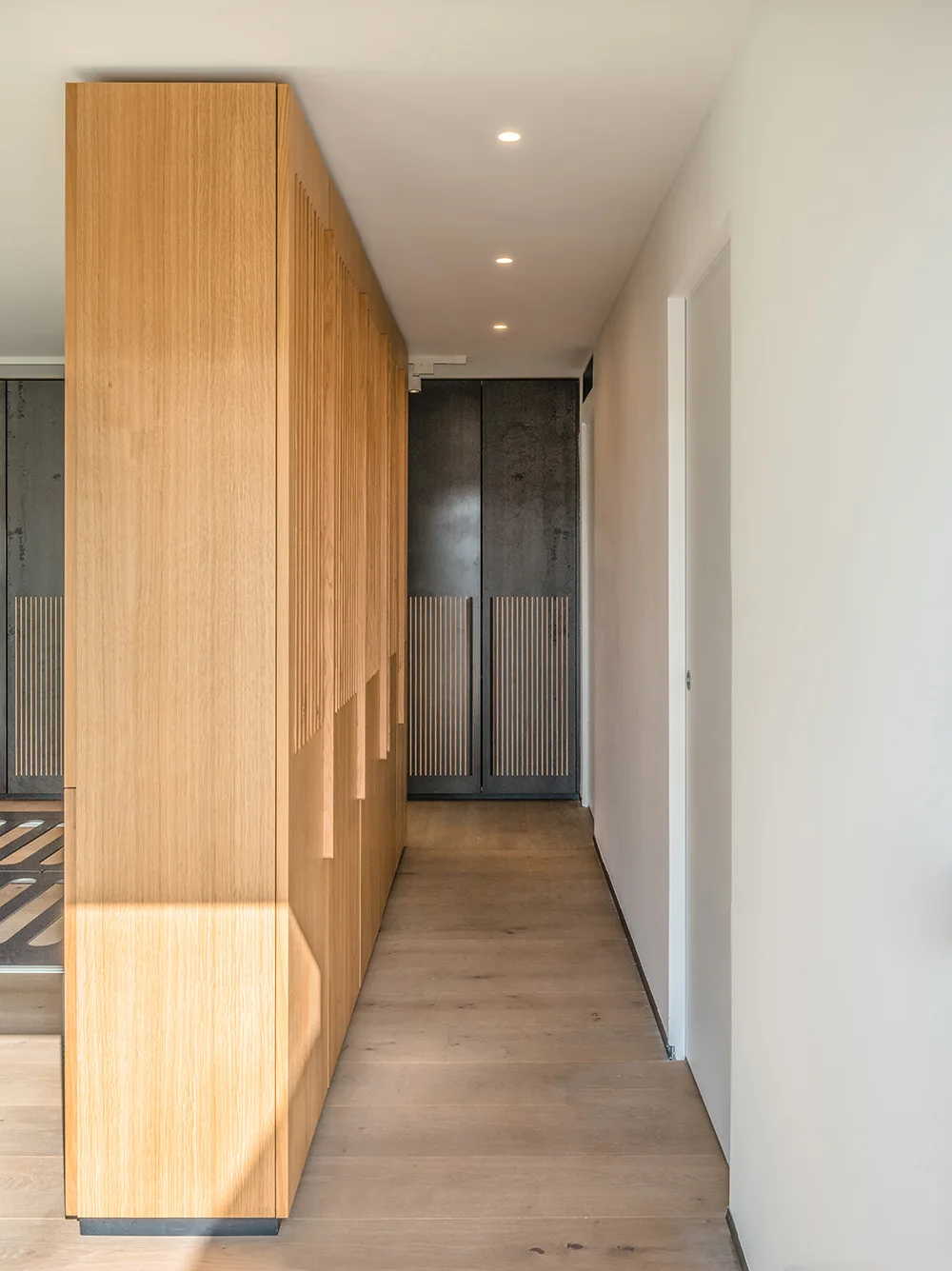A narrow white hallway features a large floor-to-ceiling light wood storage cabinet with vertical slatted detailing and a wood plank floor.