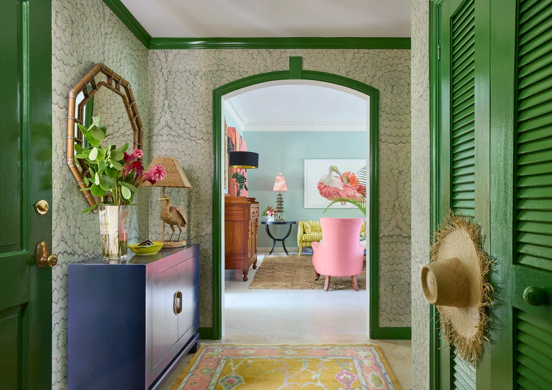 A vibrant entryway with green patterned wallpaper, high-gloss green trim, a blue console table, and an archway opening to a living room.
