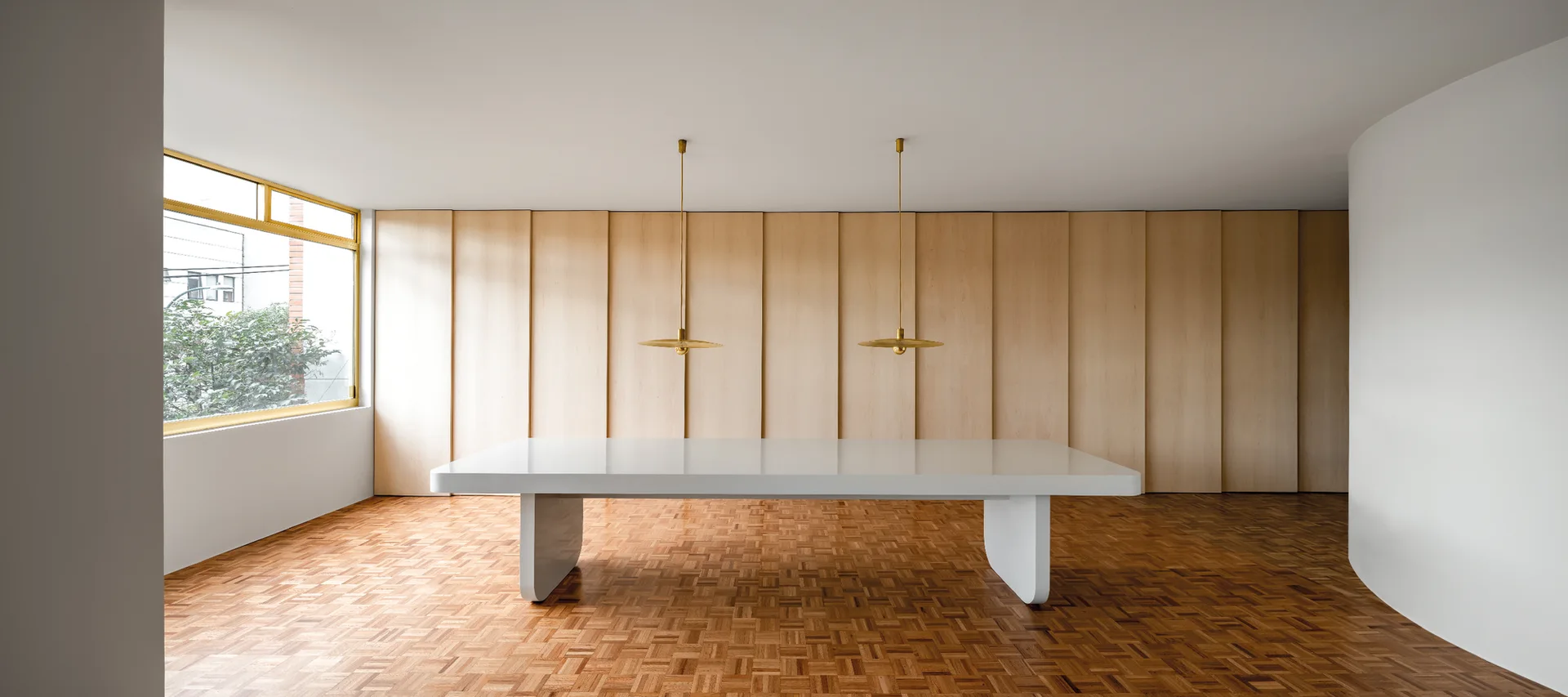 A minimalist dining room featuring a large glossy white dining table set against vertical wood wall paneling and a parquet wood floor.