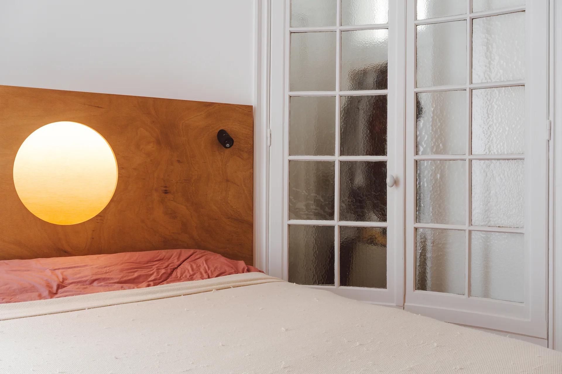 A bedroom corner features a wooden headboard with an illuminated circular cutout next to white French doors with textured glass panes.