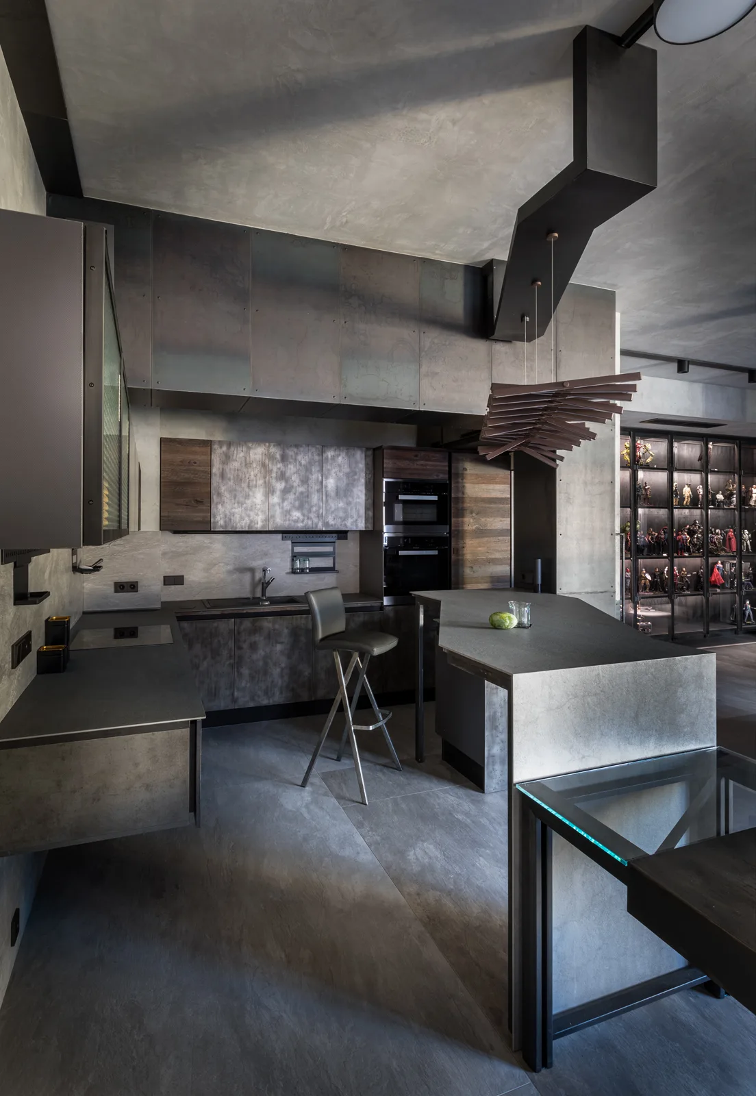 A moody industrial kitchen with dark metal cabinets, a textured stone island, and a glass-front display cabinet filled with figurines.