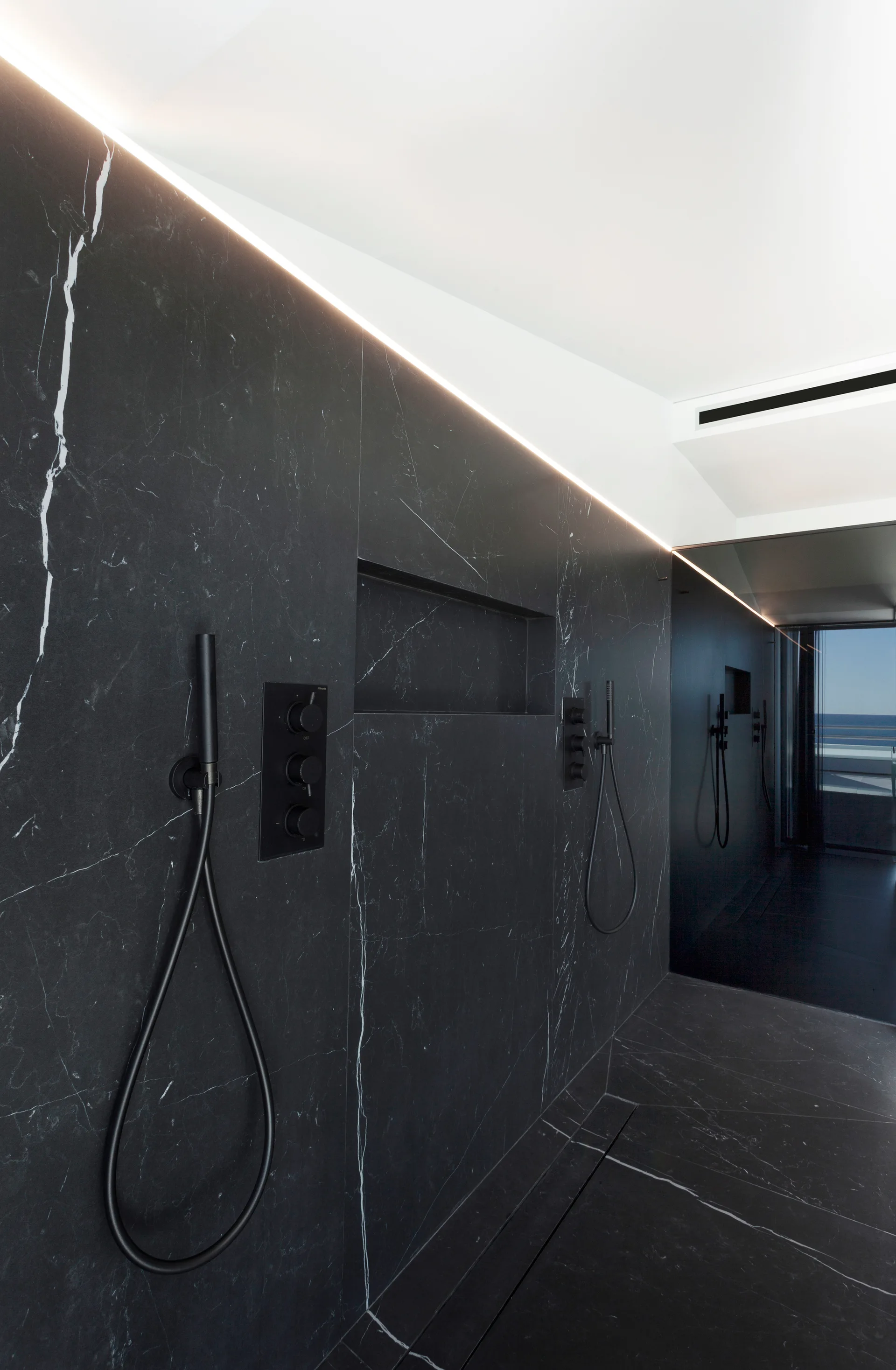 A modern walk-in shower featuring dark black marble walls and floor with white veining, black matte fixtures, and a recessed wall niche.