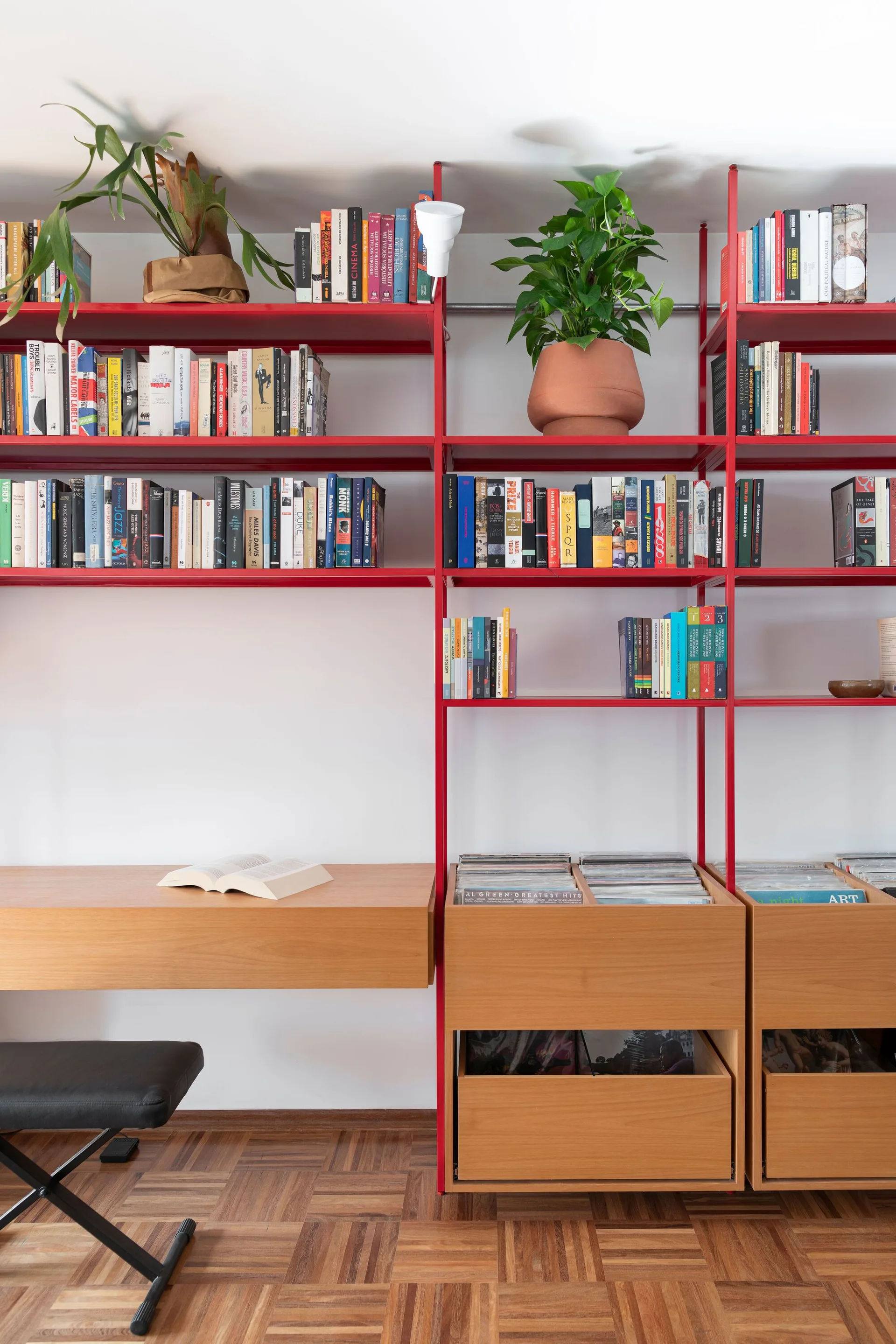A bright red metal shelving unit with an integrated wood desk and record storage bins stands against a white wall on parquet floors.