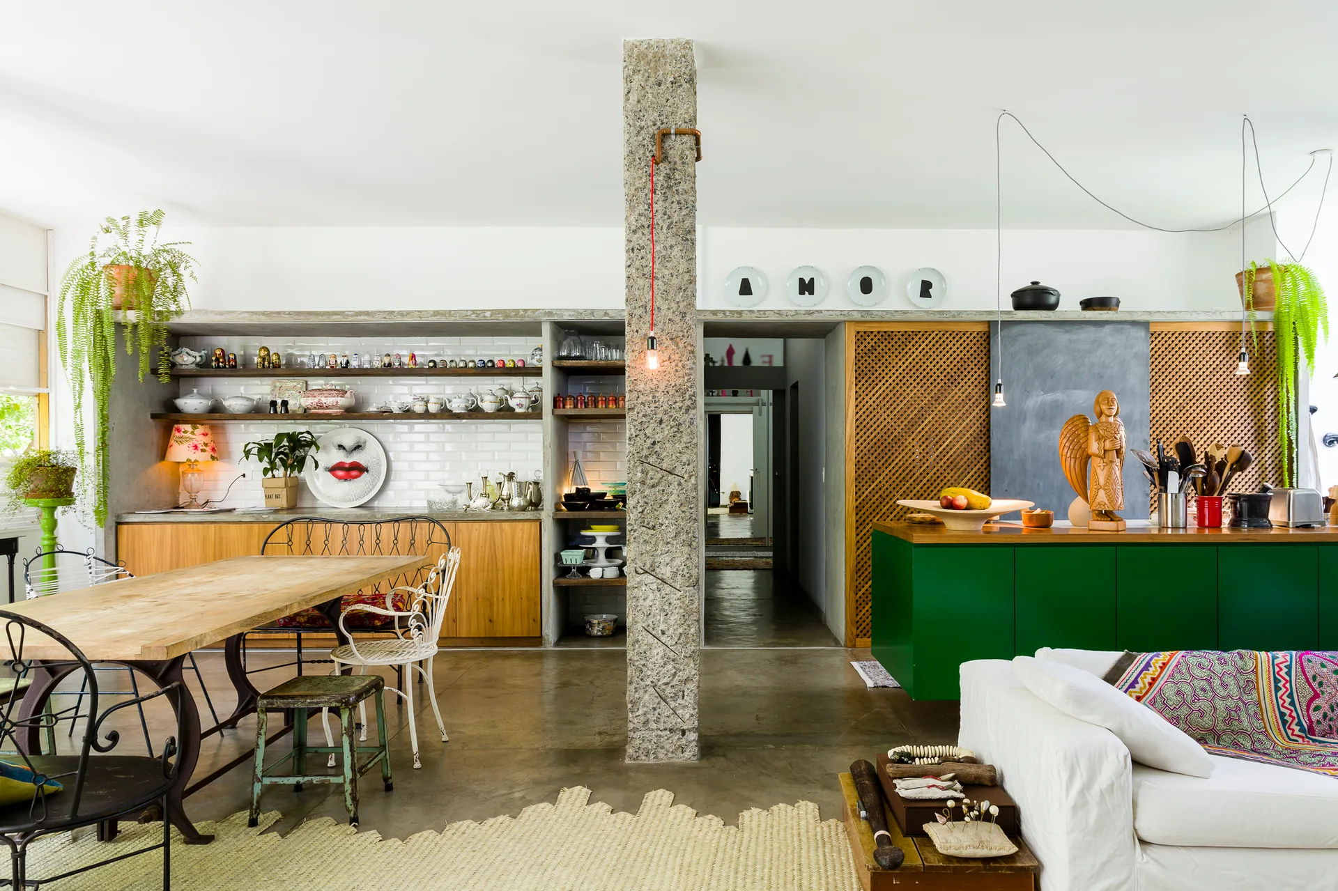 An open-plan kitchen and dining space featuring a textured granite column, a green kitchen island, and a wooden dining table.