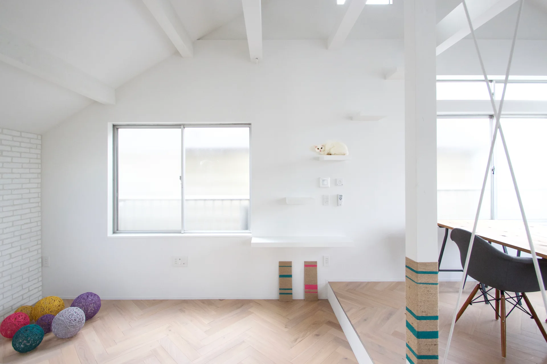A minimalist white room with herringbone wood floors, white floating cat shelves on the wall, and a support column wrapped in striped rope.