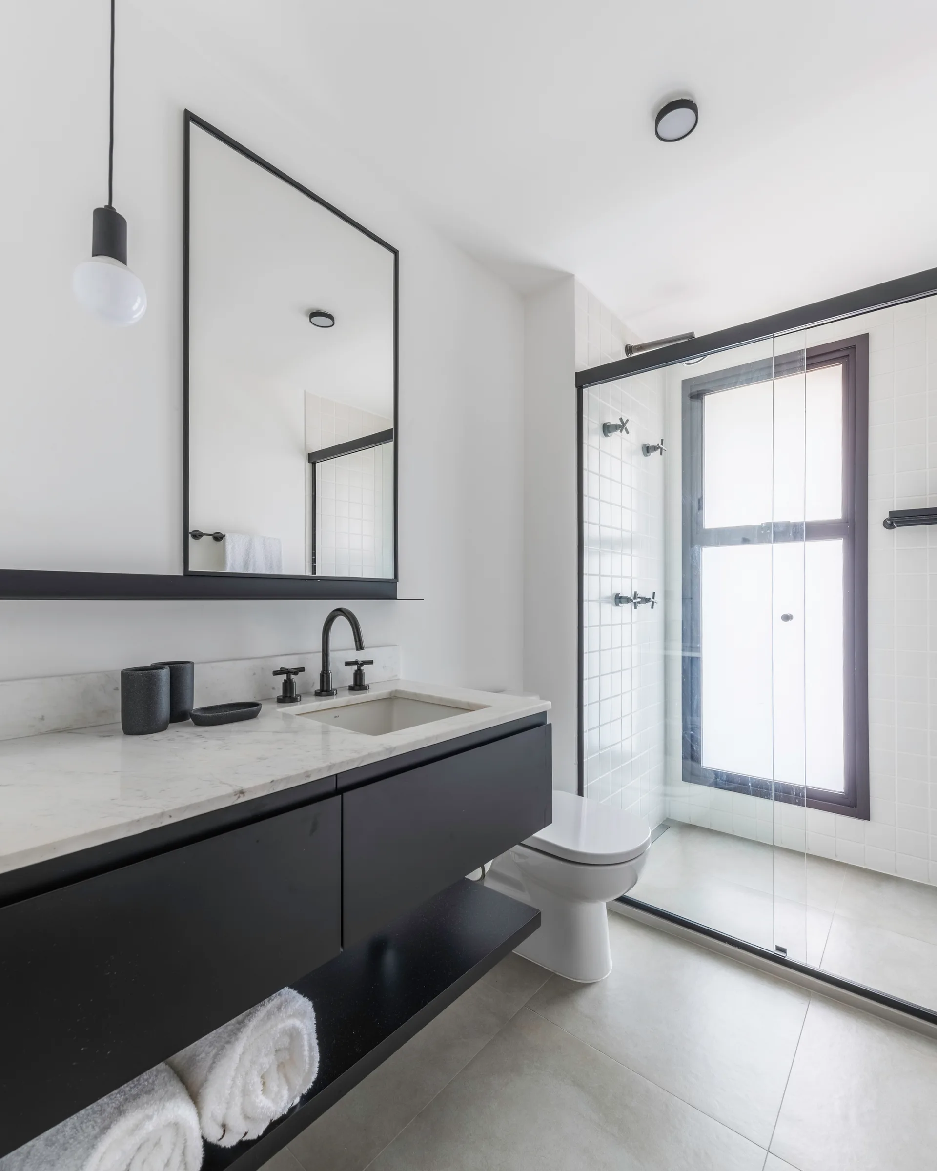 A modern bathroom features a floating black vanity with a marble top, a black-framed mirror, and a glass shower enclosure with white square tiles.