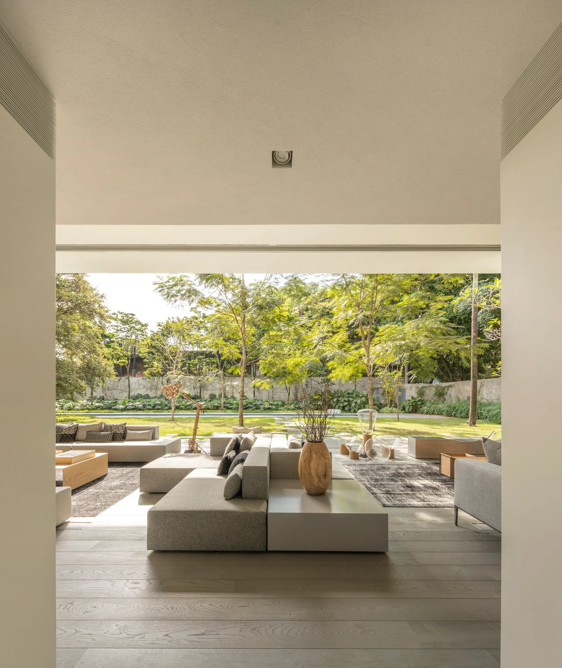 A covered grey patio features a low-profile modular sectional sofa and a wooden vase overlooking a lush green garden lawn.