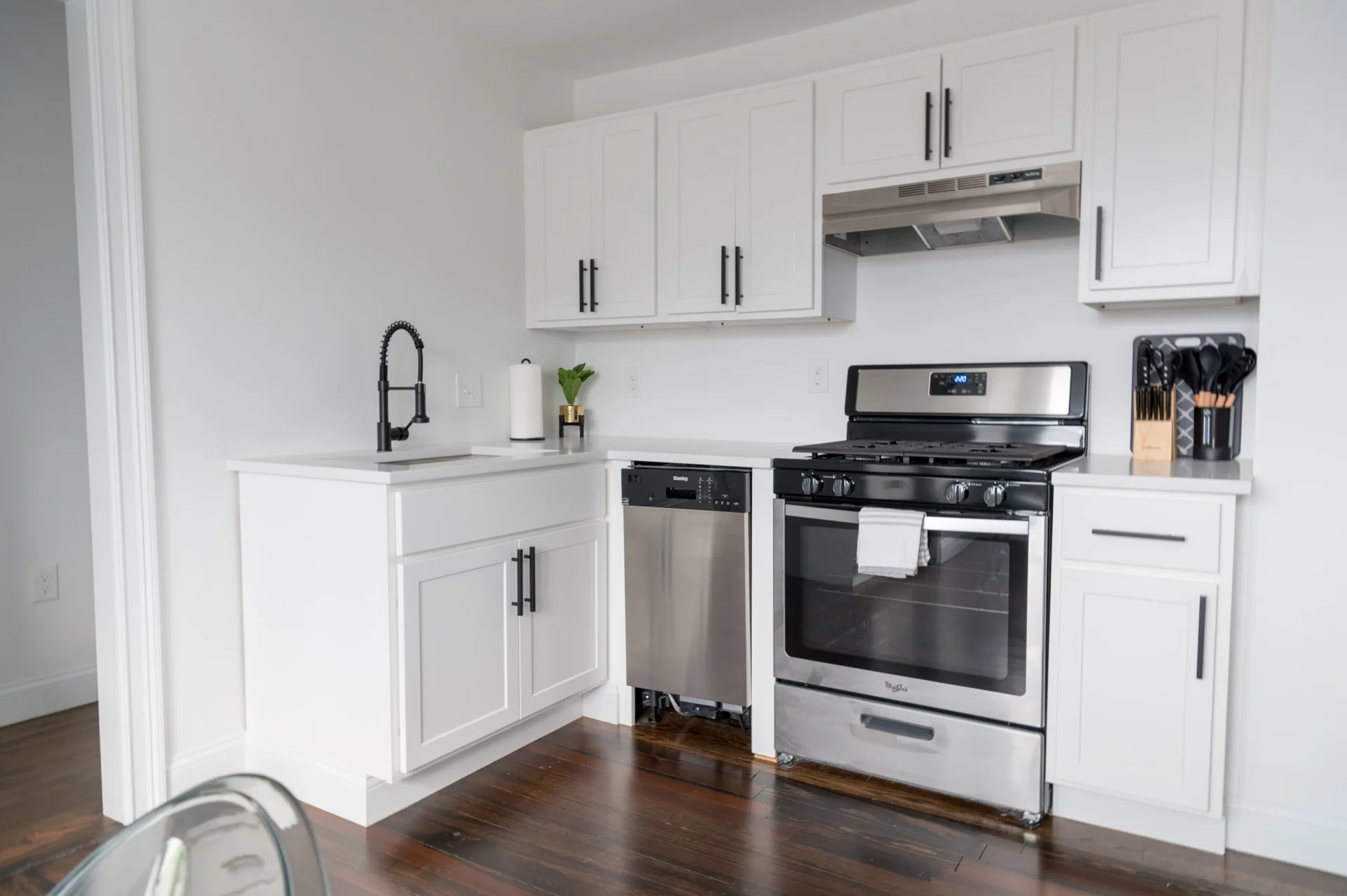 A modern kitchen featuring white shaker cabinets with black pulls, a matte black gooseneck faucet, stainless steel appliances, and dark wood floors.