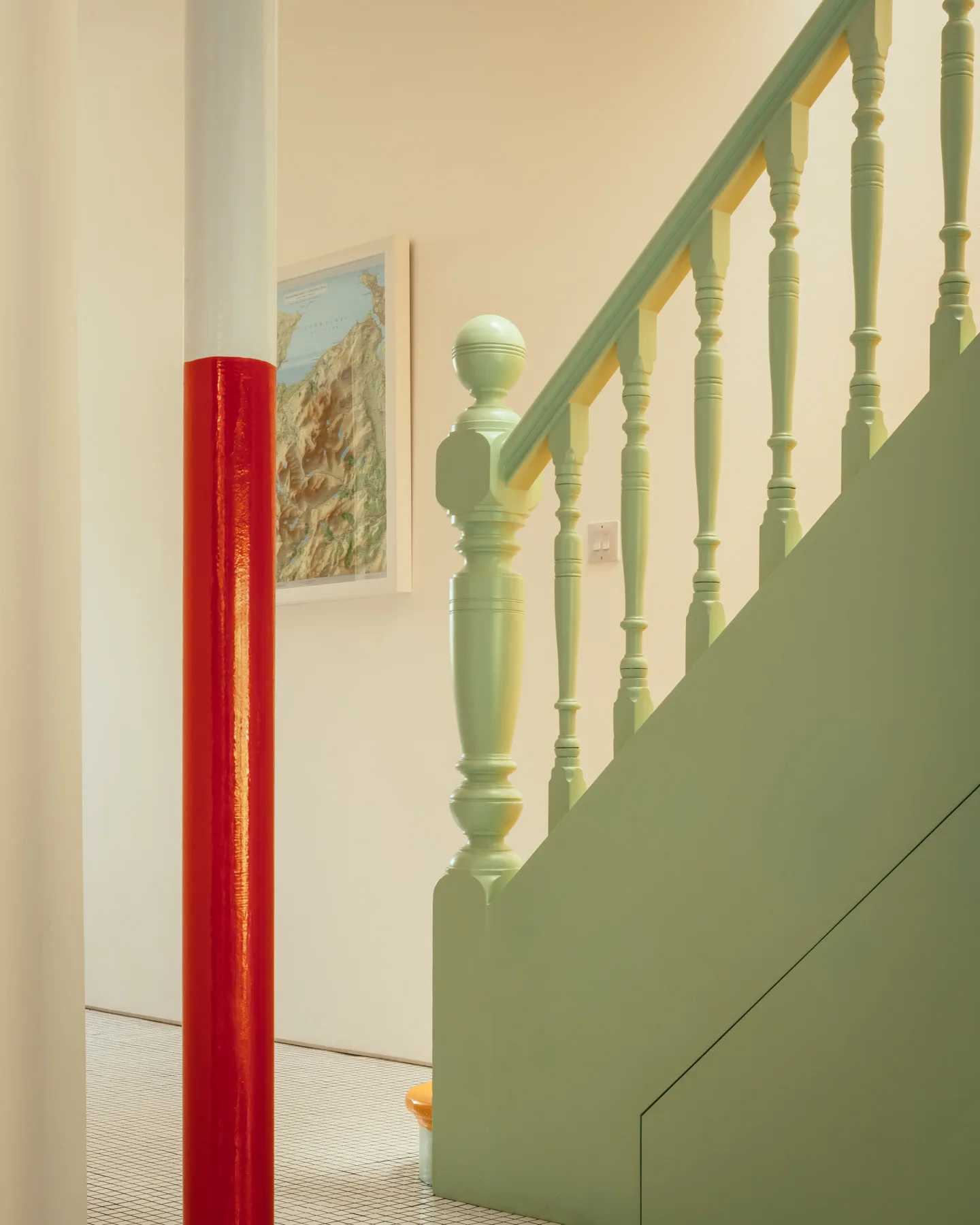 A mint green painted wooden staircase stands near a gloss red and white structural column on small white grid floor tiles.