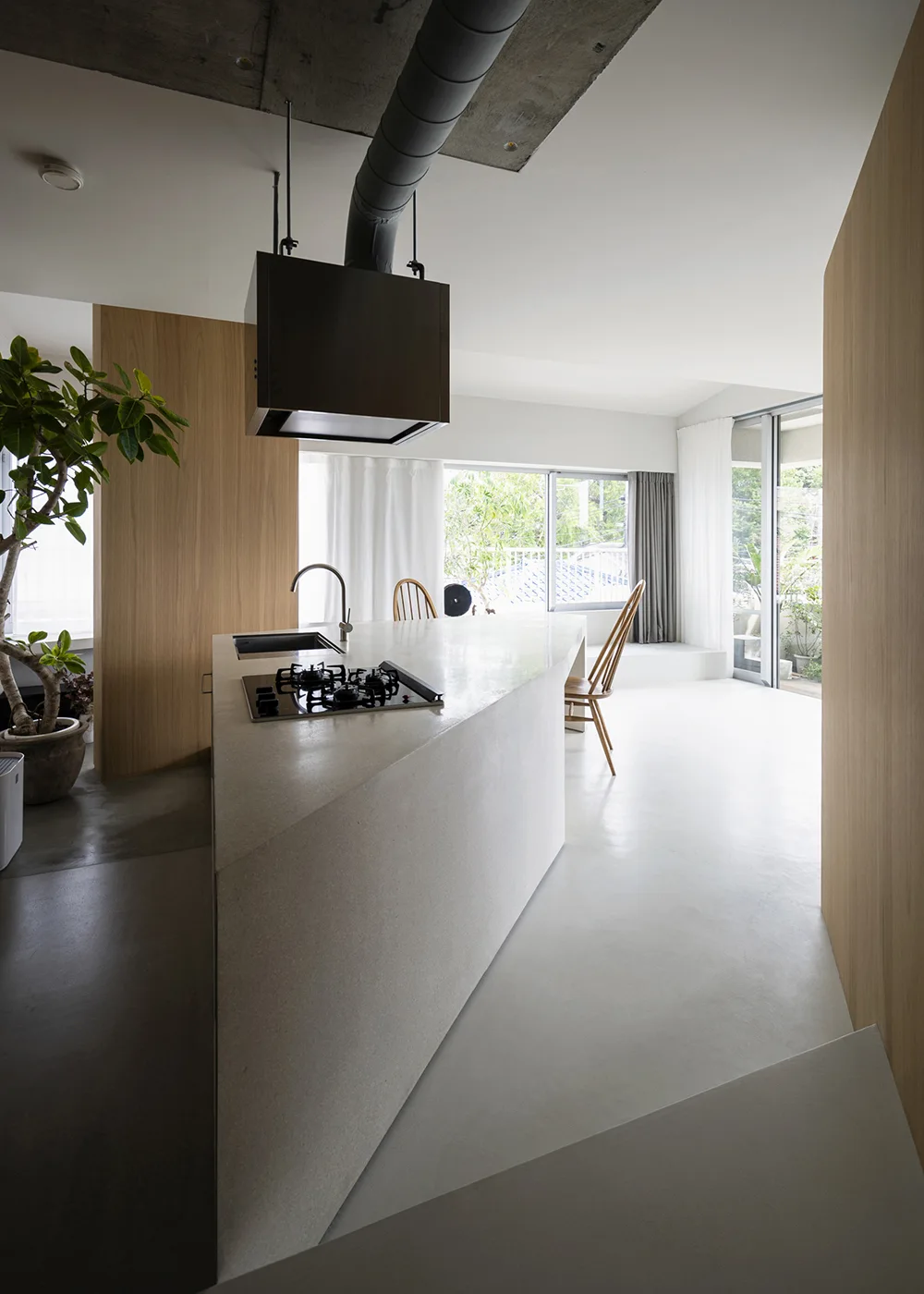 A modern minimalist kitchen featuring a large angular concrete-look island, light wood-paneled walls, and an industrial raw concrete ceiling.