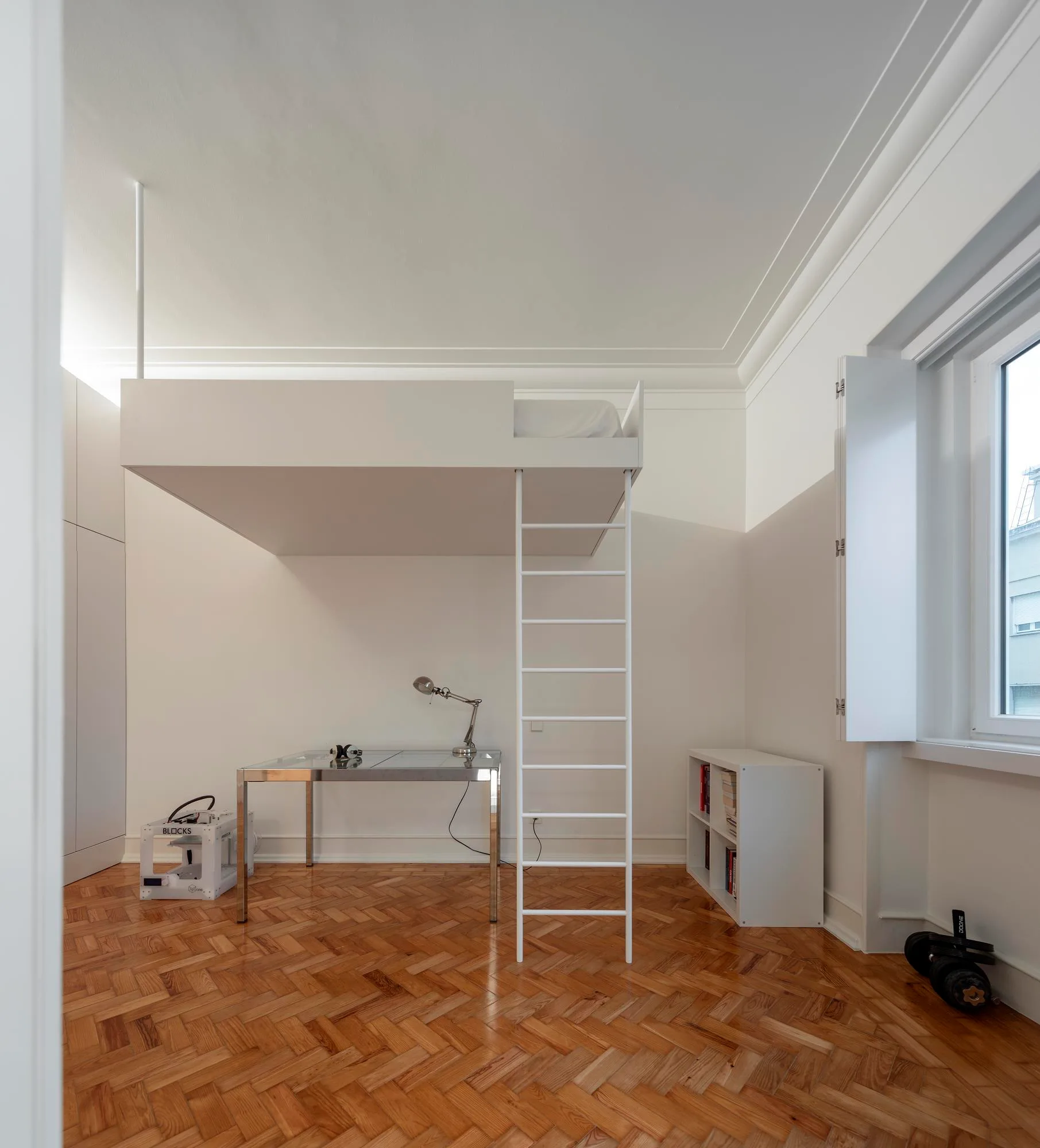 A white loft bed with a ladder sits above a metal-framed desk on a rich wood herringbone parquet floor in a minimalist room.