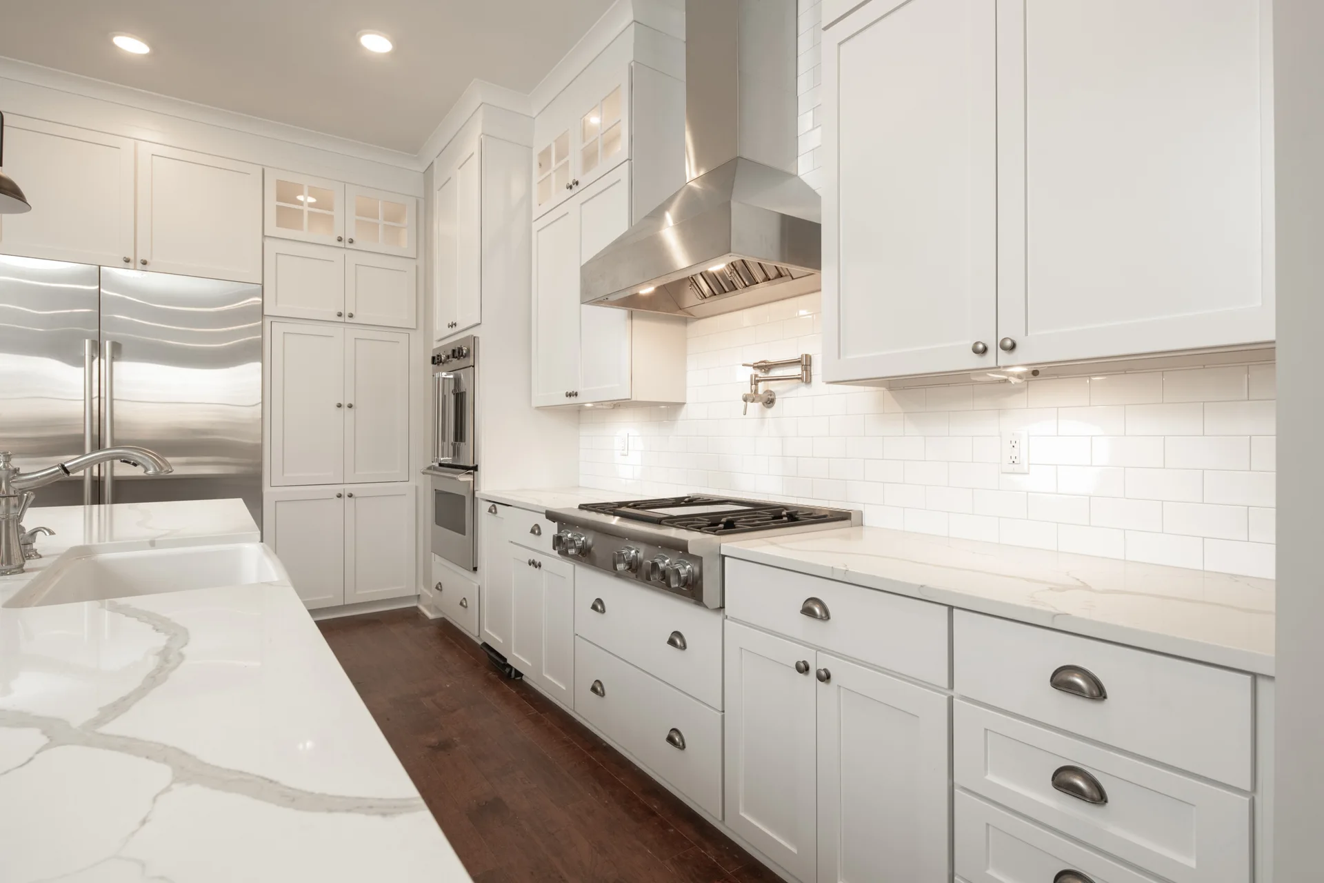 A bright white kitchen features shaker-style cabinets, a stainless steel range hood, marble countertops, and a subway tile backsplash.