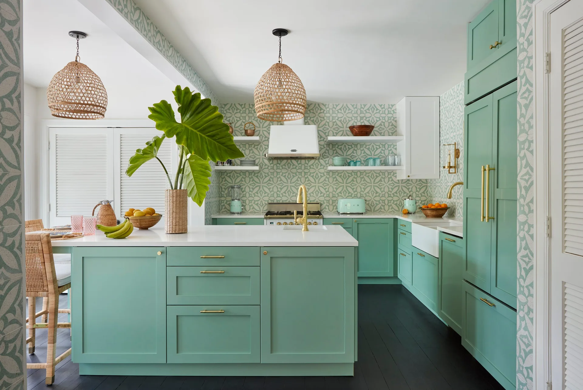 A bright kitchen features mint green cabinetry, a matching geometric wallpaper backsplash, white countertops, and woven rattan pendant lights.