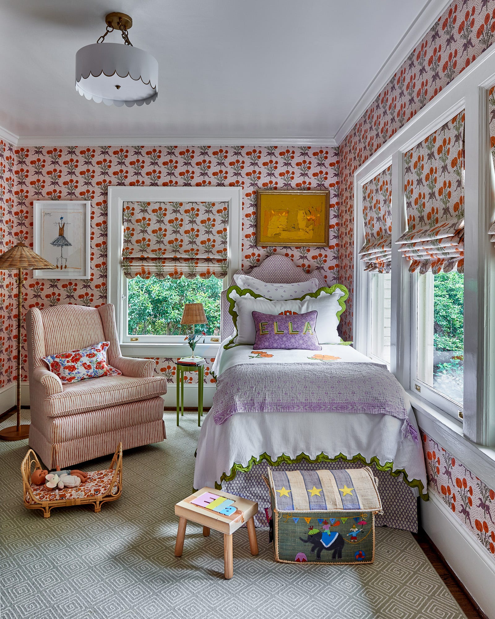 A child's bedroom features orange floral wallpaper matching the roman shades, a single bed with purple and green accents, and a striped armchair.