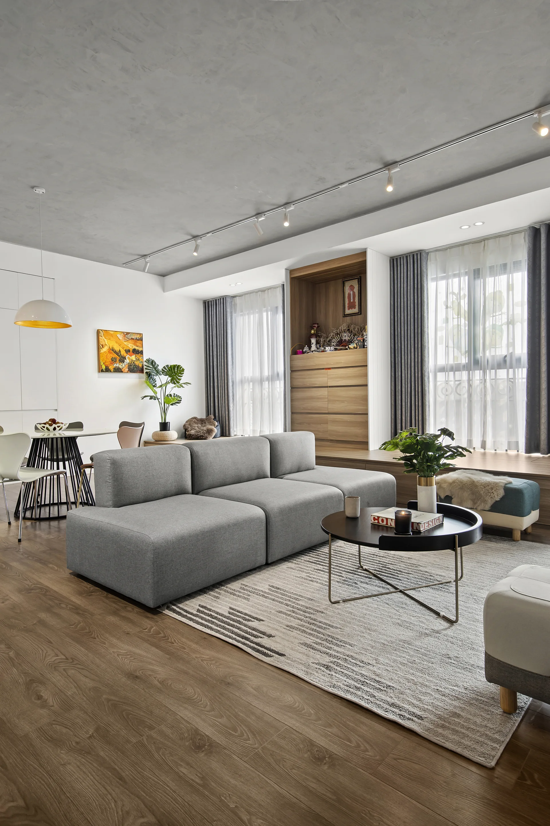 A modern living room features a grey modular sofa, a round black coffee table on a patterned rug, and a textured grey concrete ceiling with track lighting.