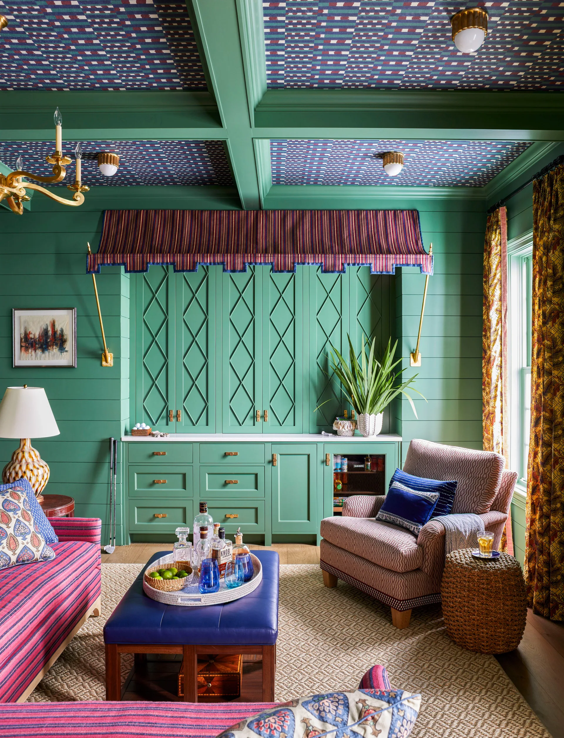 A home bar features green built-in cabinets and shiplap walls under a coffered ceiling lined with patterned wallpaper.