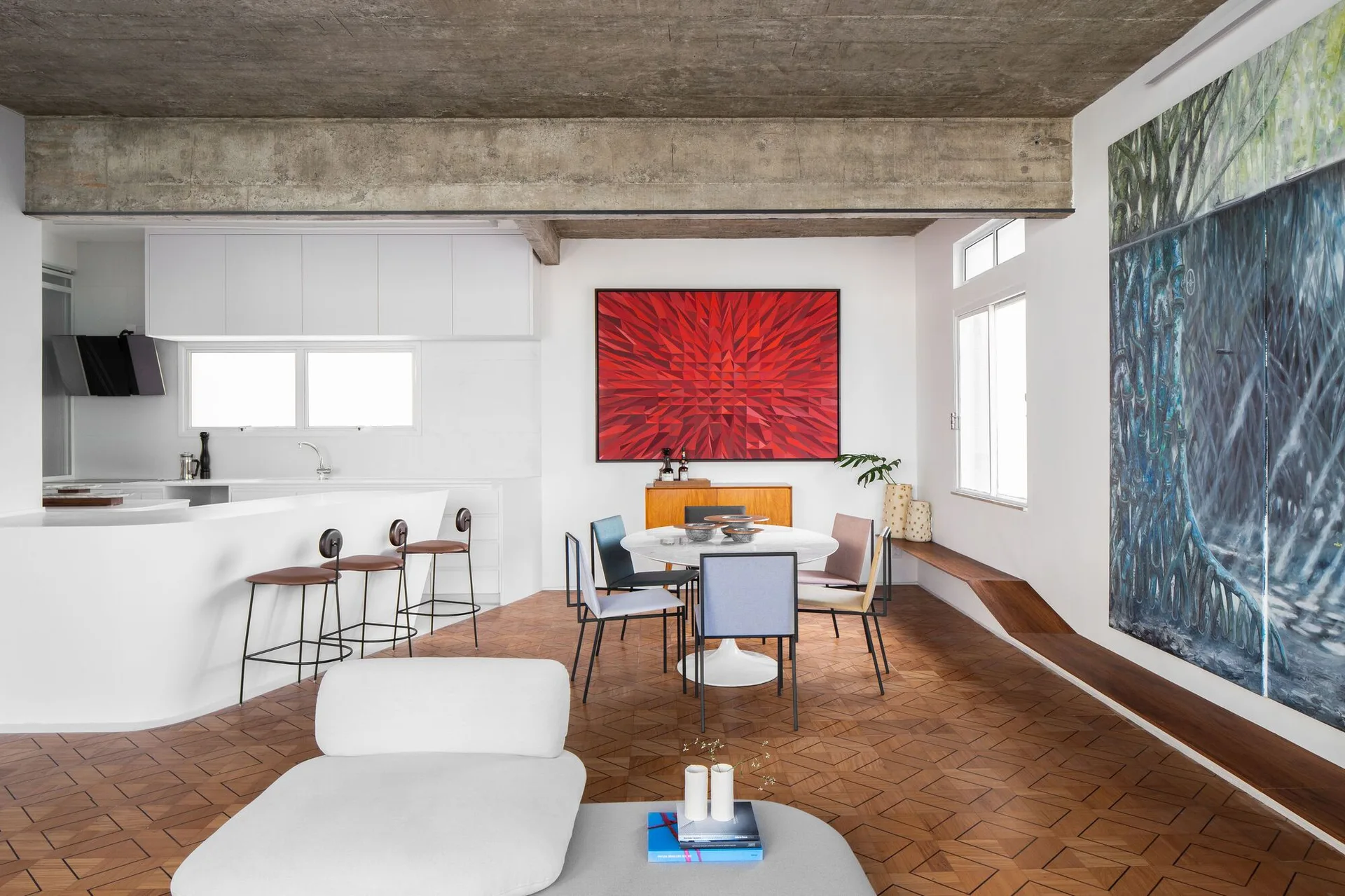 An open dining space featuring a round table with chairs, a curved white kitchen island, geometric wood flooring, and an exposed concrete ceiling.