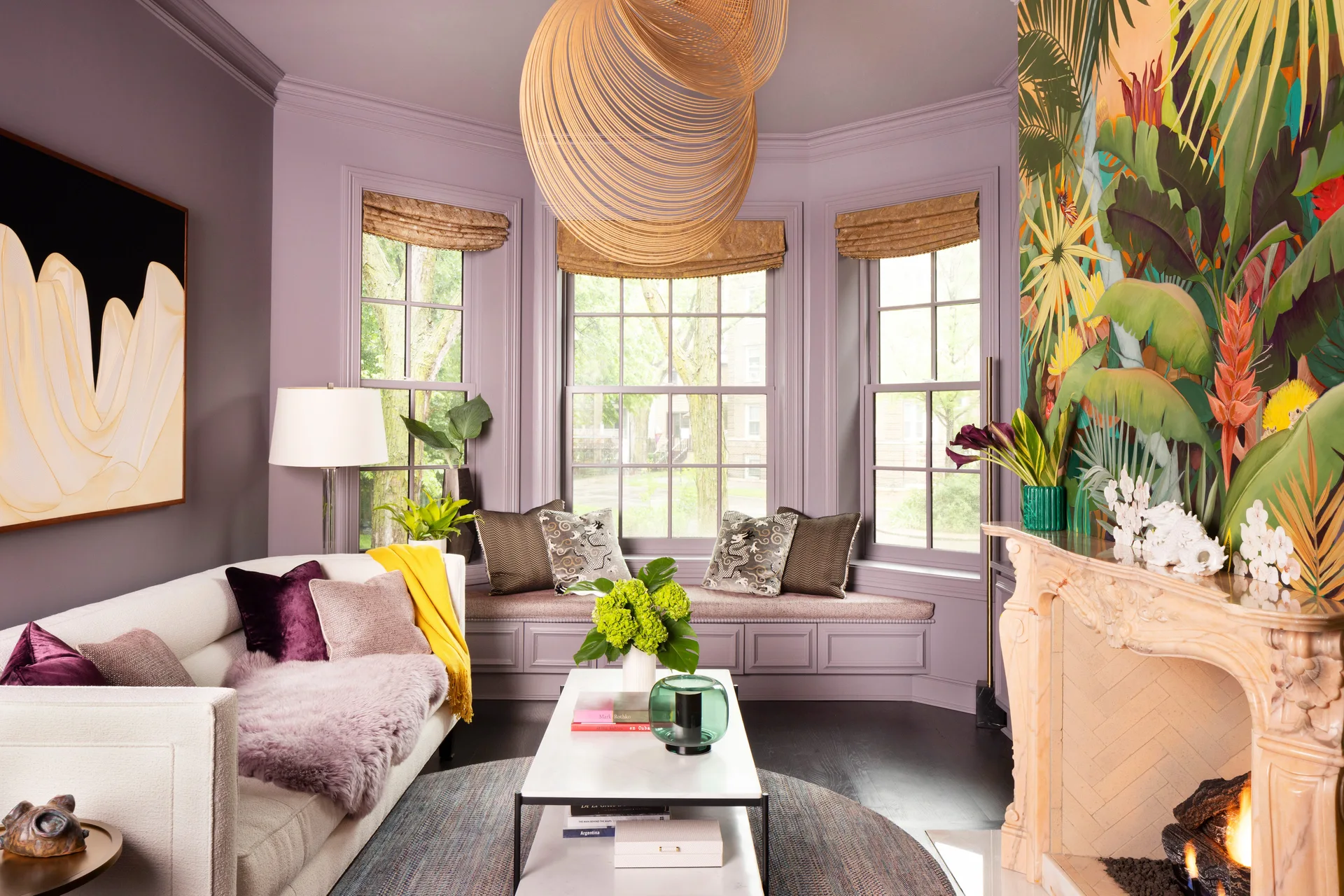 A lilac living room featuring a cream sofa, an ornate stone fireplace next to a tropical mural, and a built-in bay window seat.