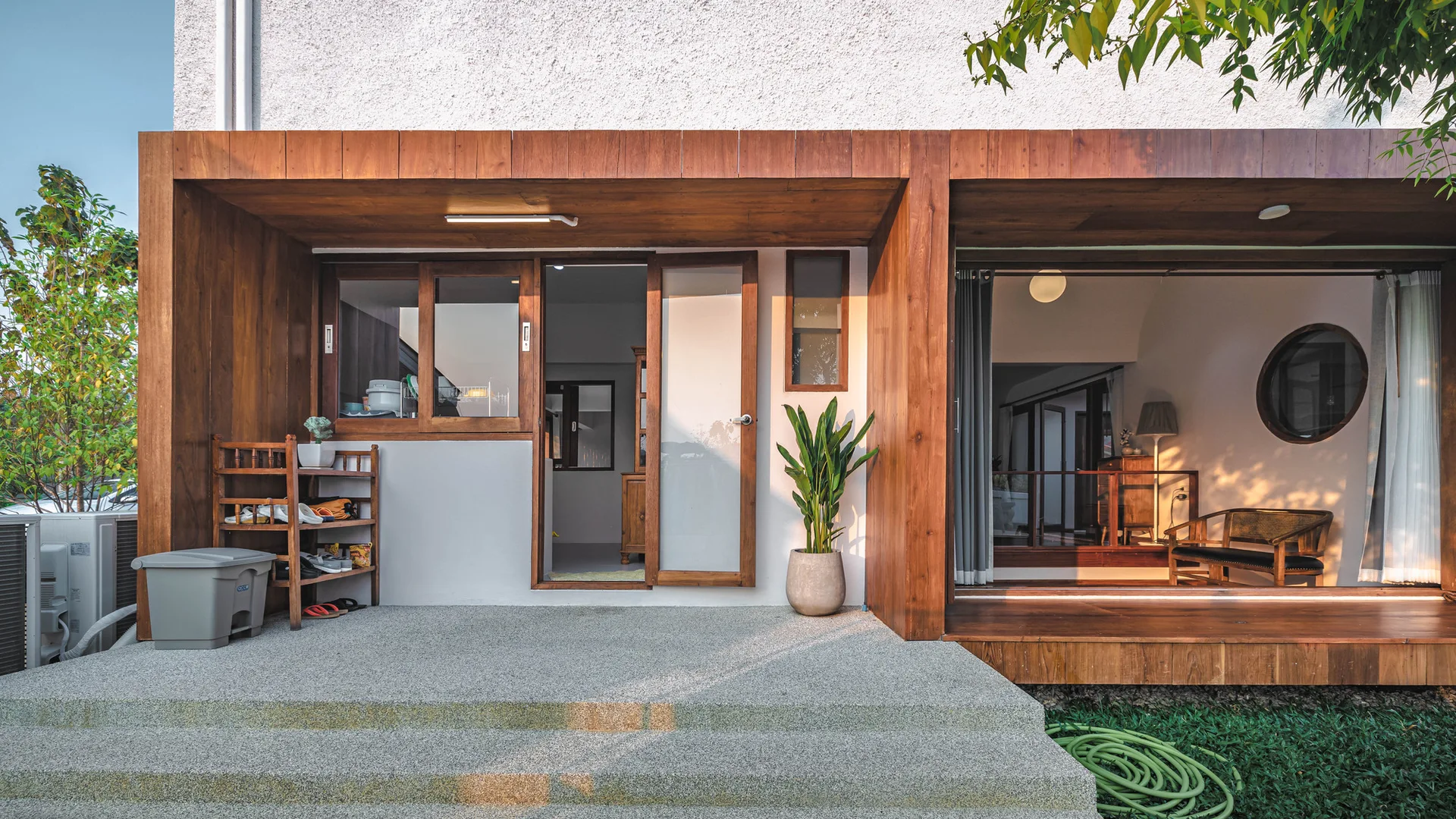 A covered residential patio features a raised textured concrete deck, warm wood panel framing, and a large sliding glass door.