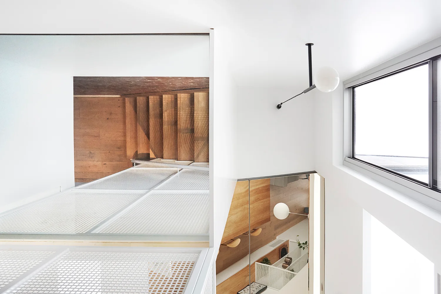 High-angle view of a minimalist white stairwell with a metal grid floor landing, wooden steps, and a globe pendant light.