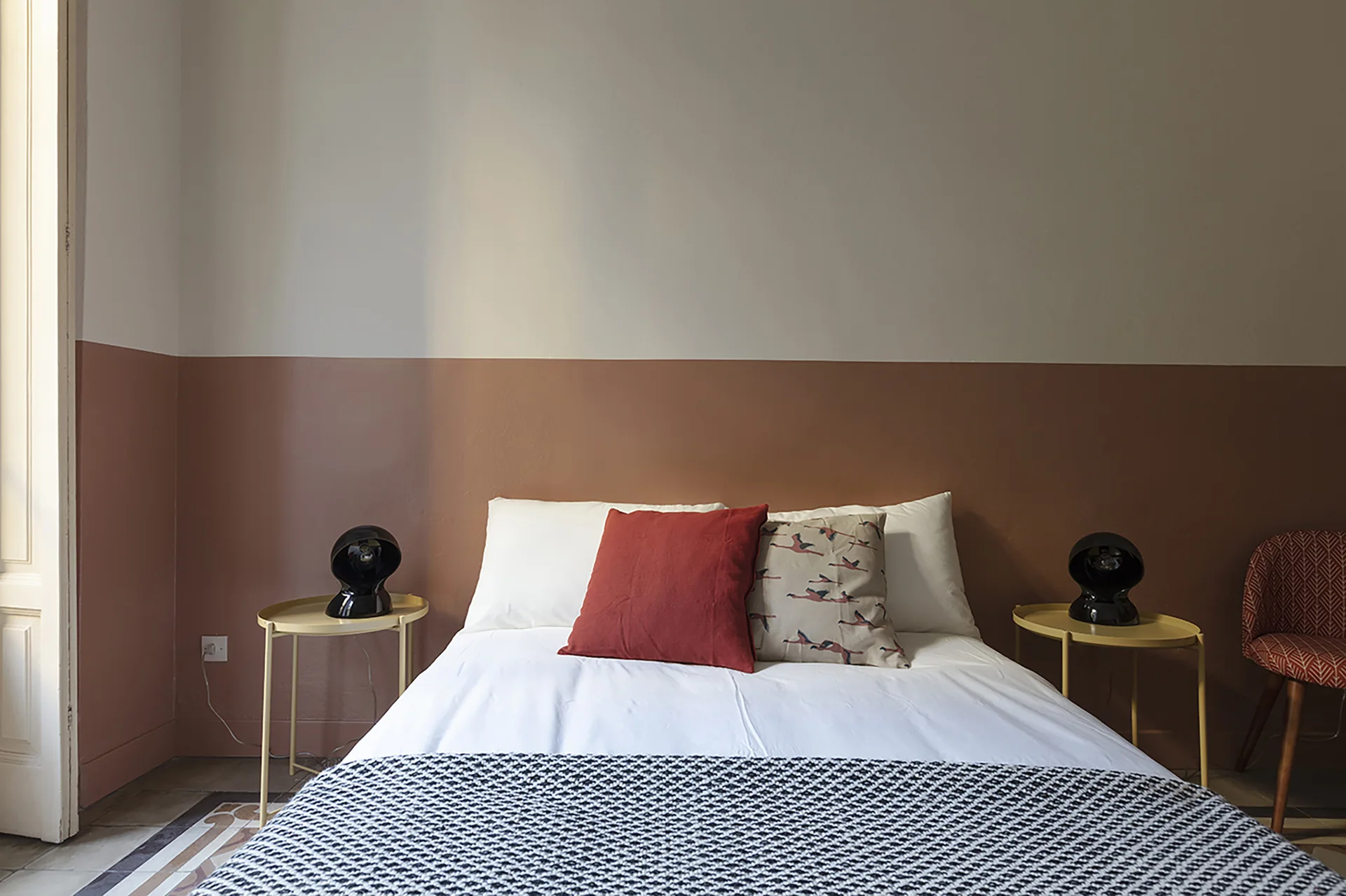 A modern bedroom features a bed with white bedding, yellow metal side tables with black spherical lamps, and a two-tone clay and white wall.