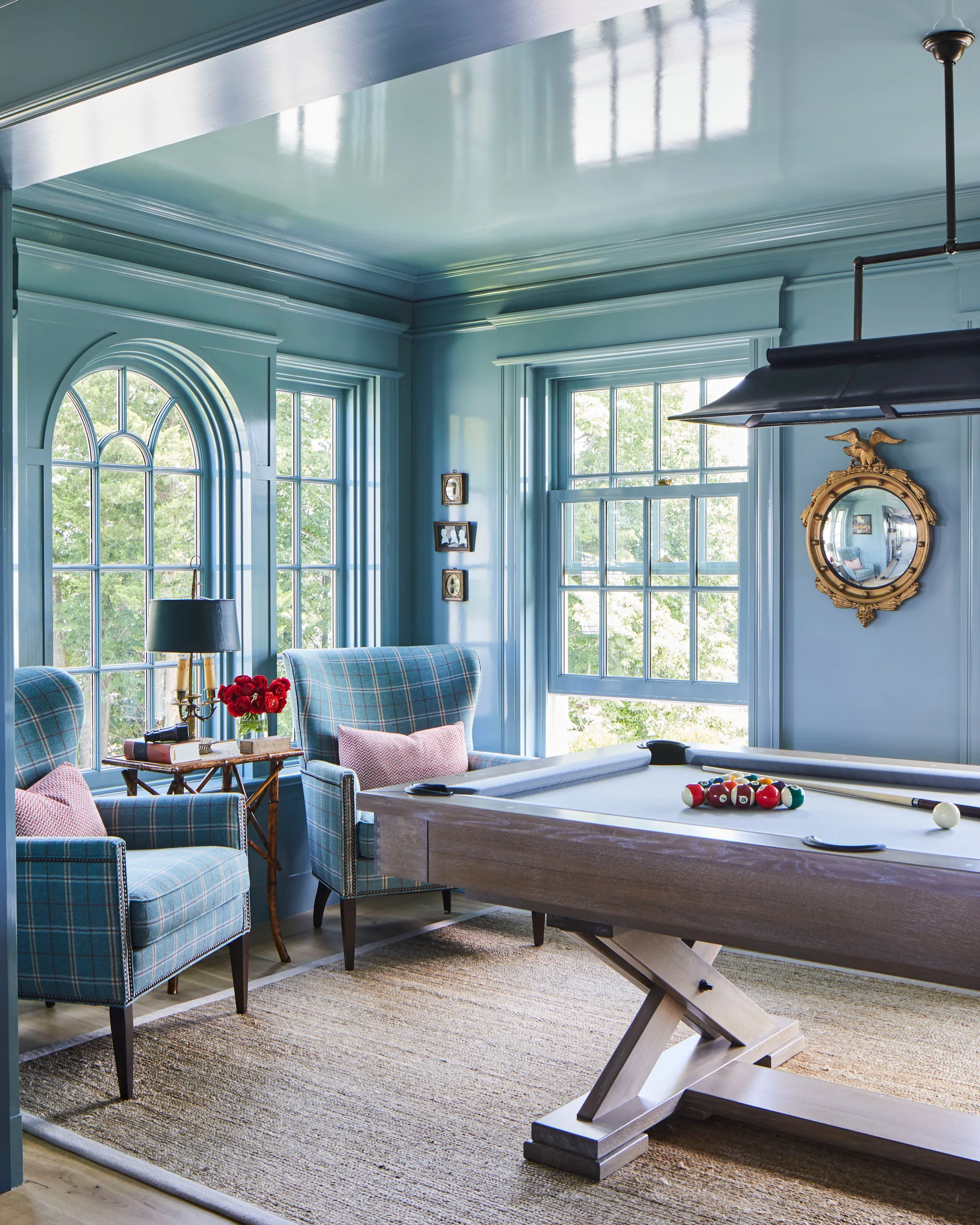 A traditional game room features a wooden billiard table, two blue plaid armchairs, and highly reflective blue paneled walls and ceiling.