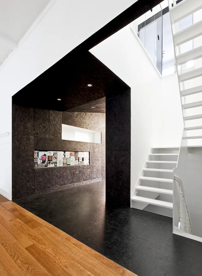 A modern white staircase stands next to a textured black alcove with a built-in art display niche, transitioning to natural wood flooring.