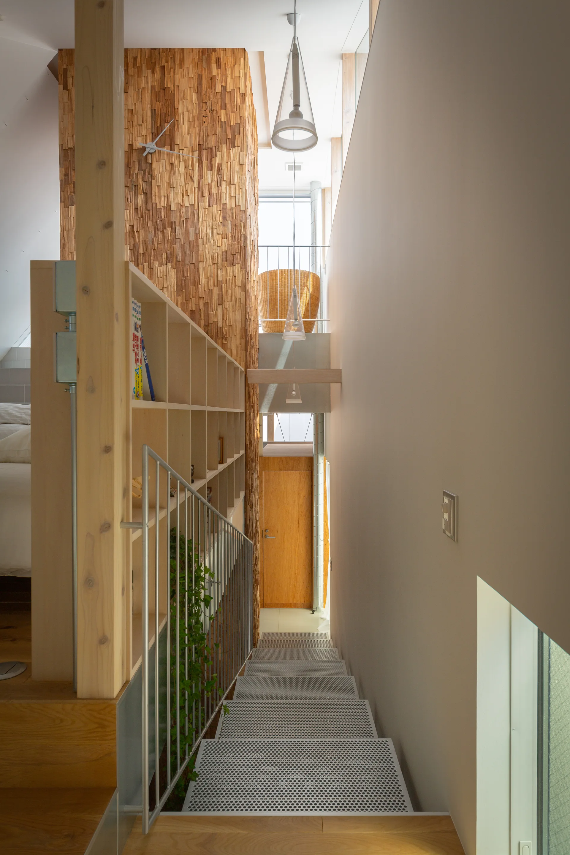 A downward view of a modern staircase featuring perforated metal steps, light wood built-in shelving, and a textured wood-block accent wall.