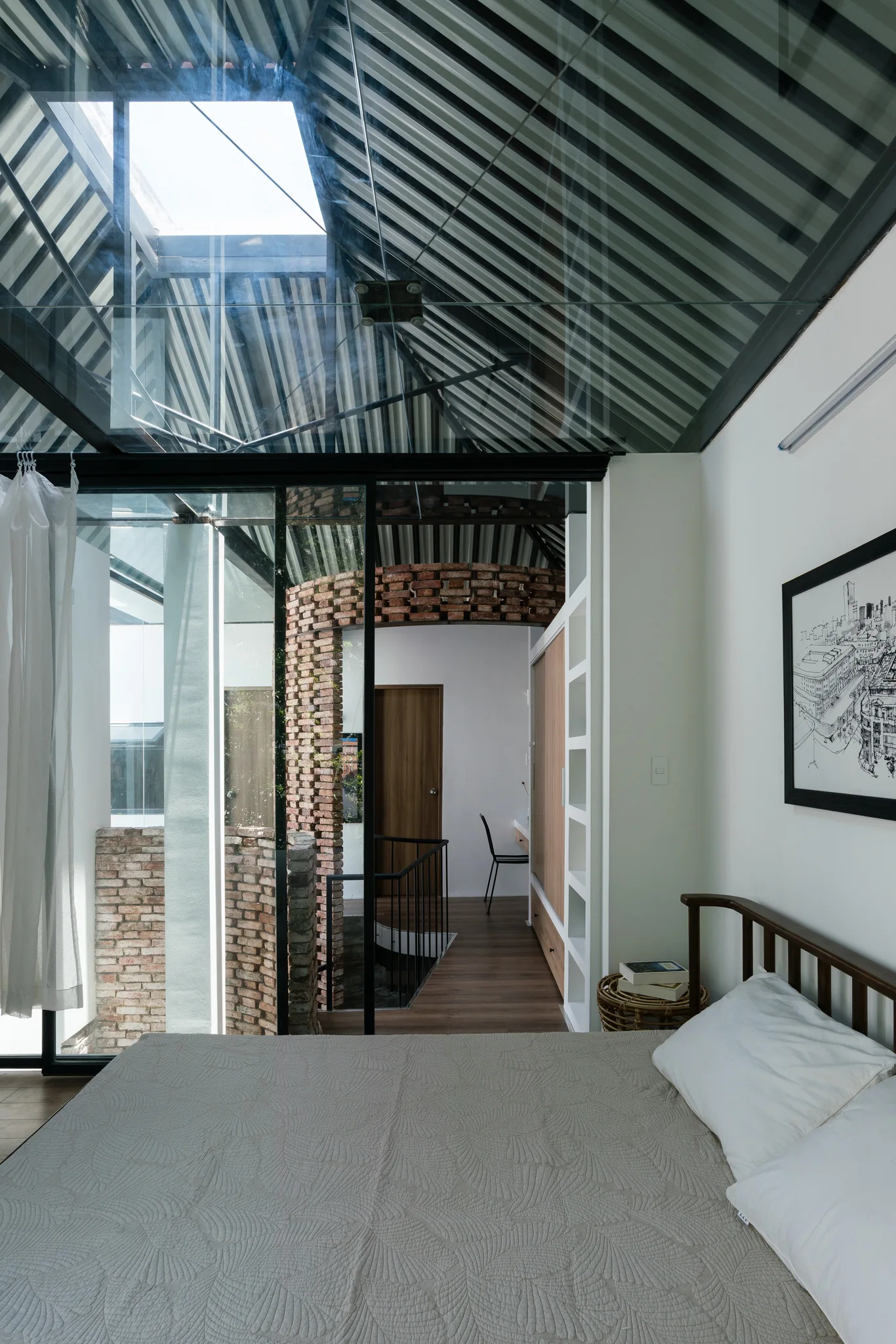 A modern bedroom features a bed with neutral quilted bedding set under a sloped glass roof skylight and a black metal frame.