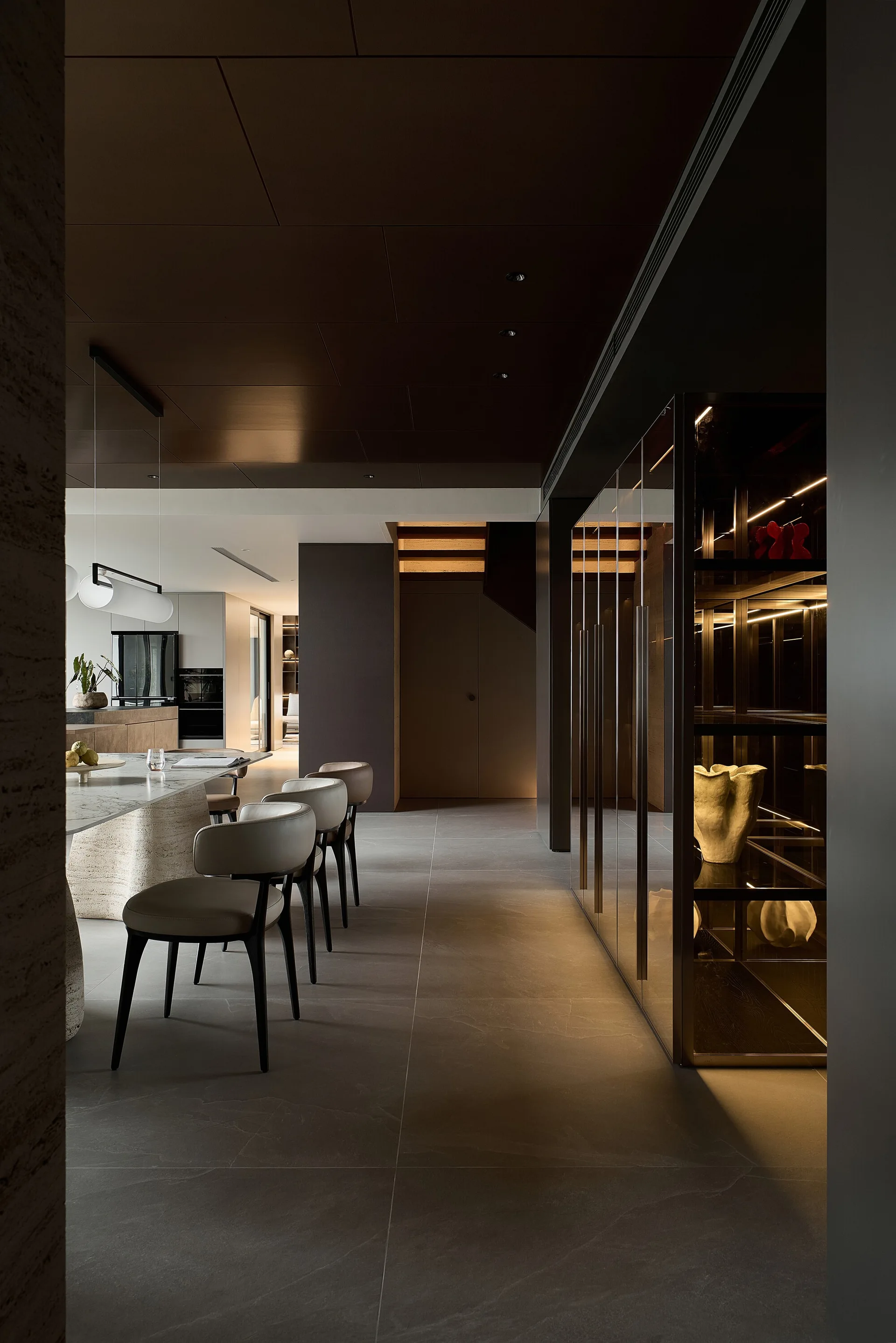 A modern dining room features a marble table with upholstered chairs next to a dark glass display cabinet with warm integrated lighting.