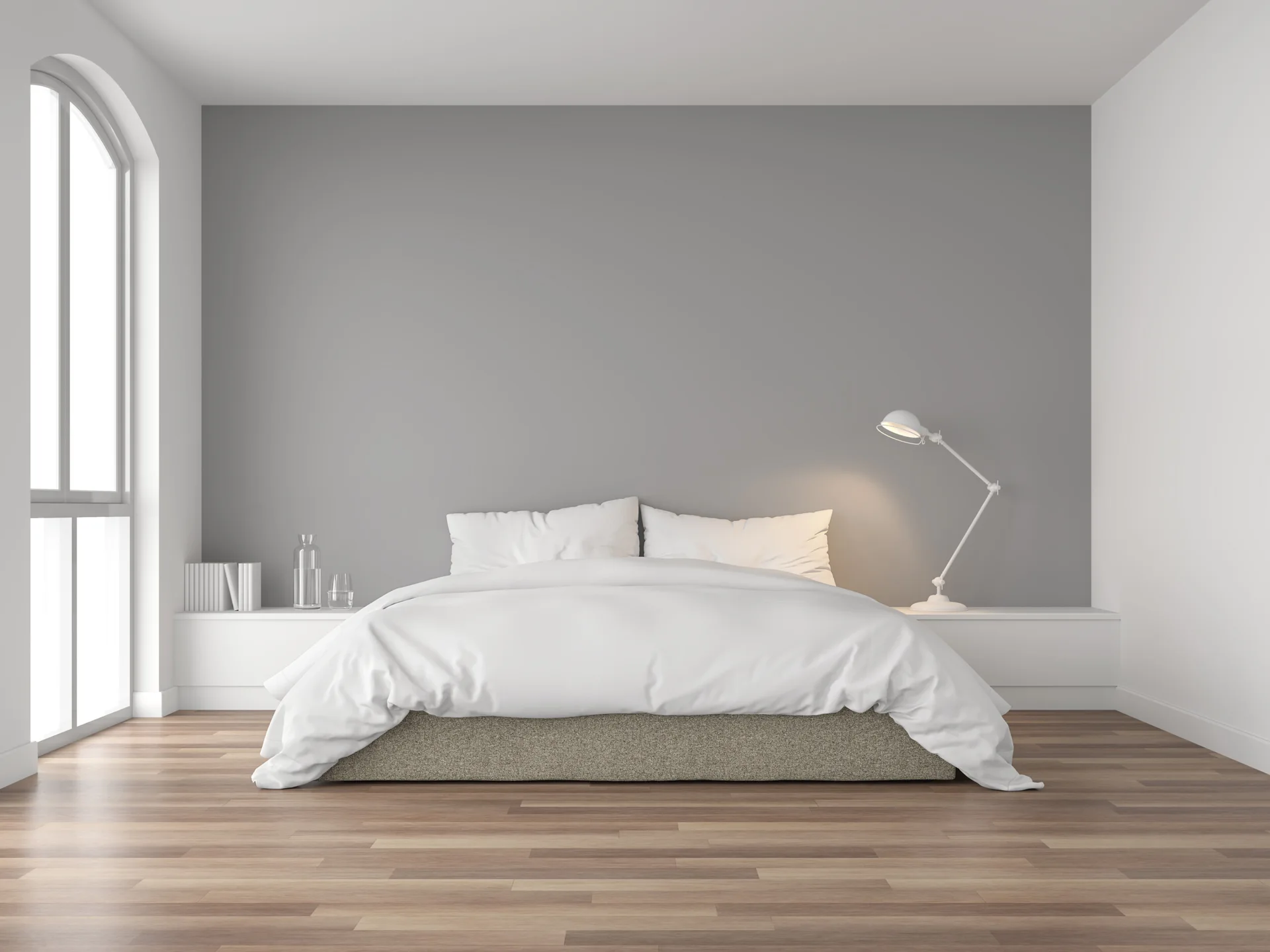 A minimalist bedroom featuring a bed centered against a grey accent wall with a white built-in ledge and an arched window.
