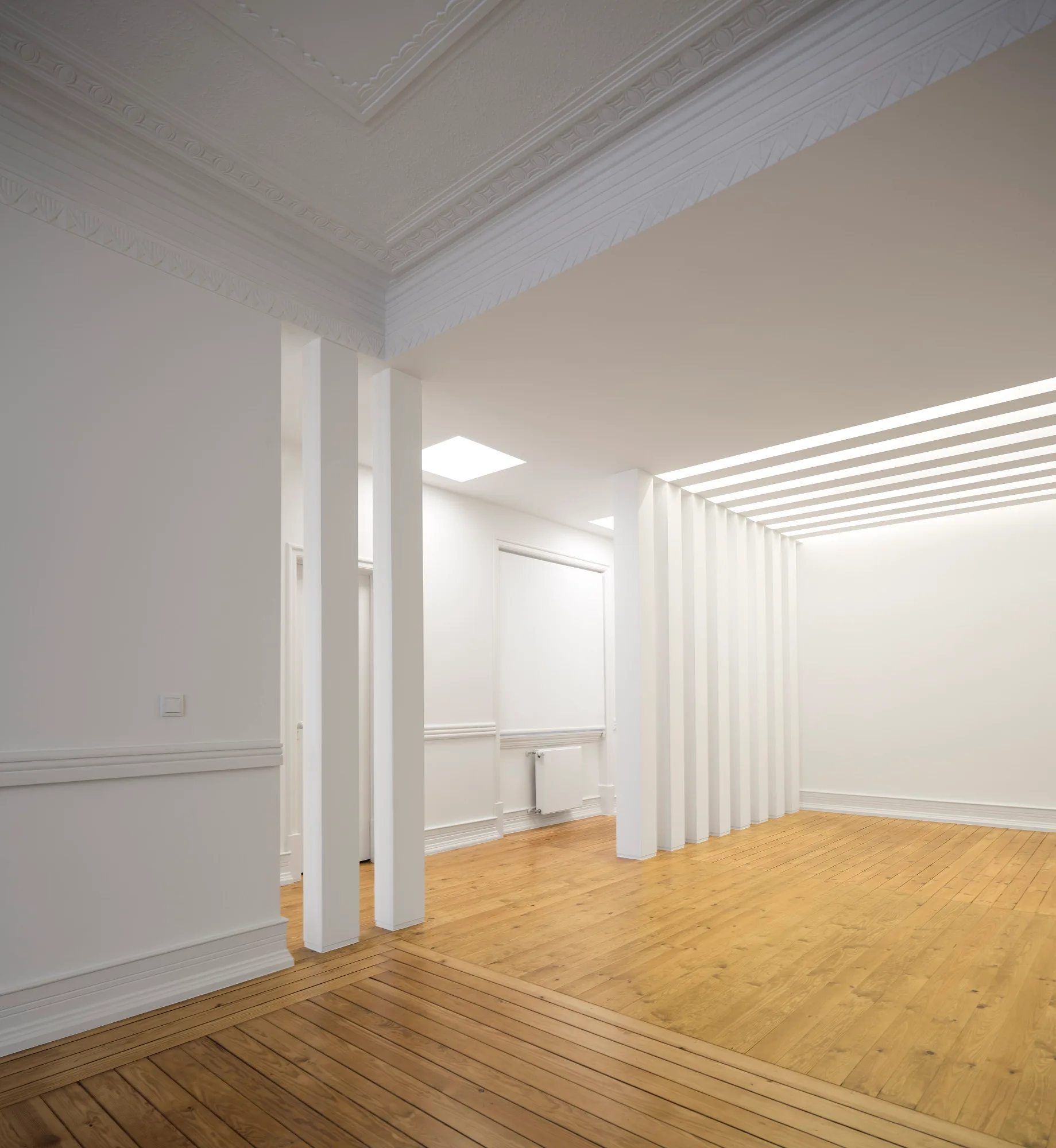 An empty white room featuring traditional crown molding, wainscoting, a vertical slat room divider, and light hardwood floors.