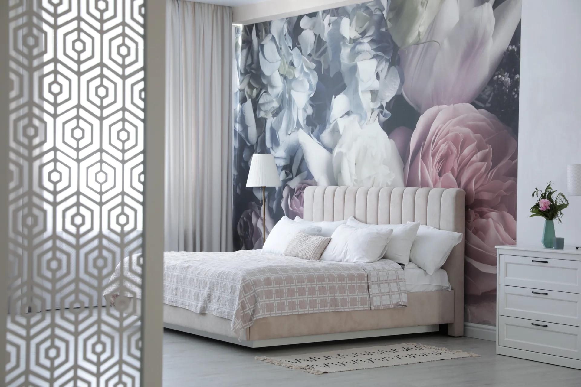 A contemporary bedroom with an upholstered bed against a large floral mural, a white dresser, and a geometric room divider screen.