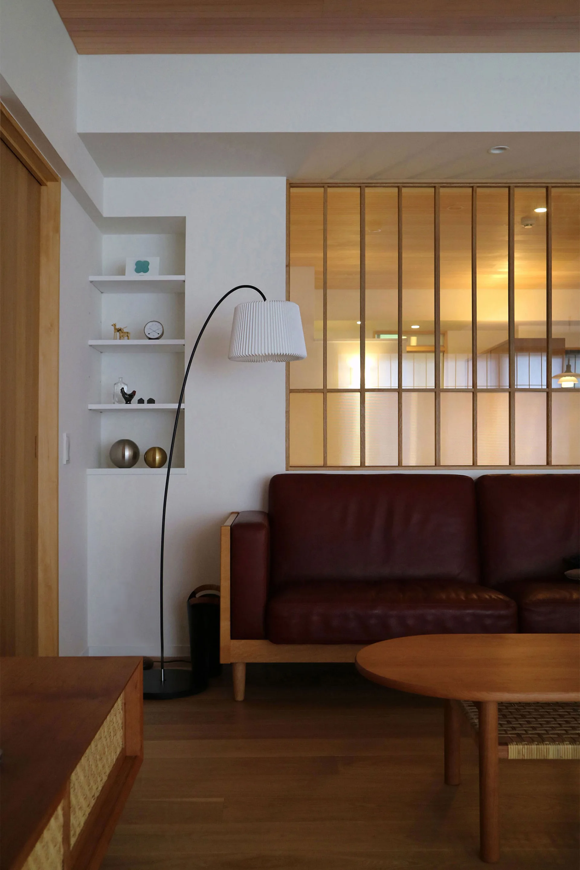 A living room features a dark red leather sofa, a curved black floor lamp, and a wood-framed glass grid partition wall.