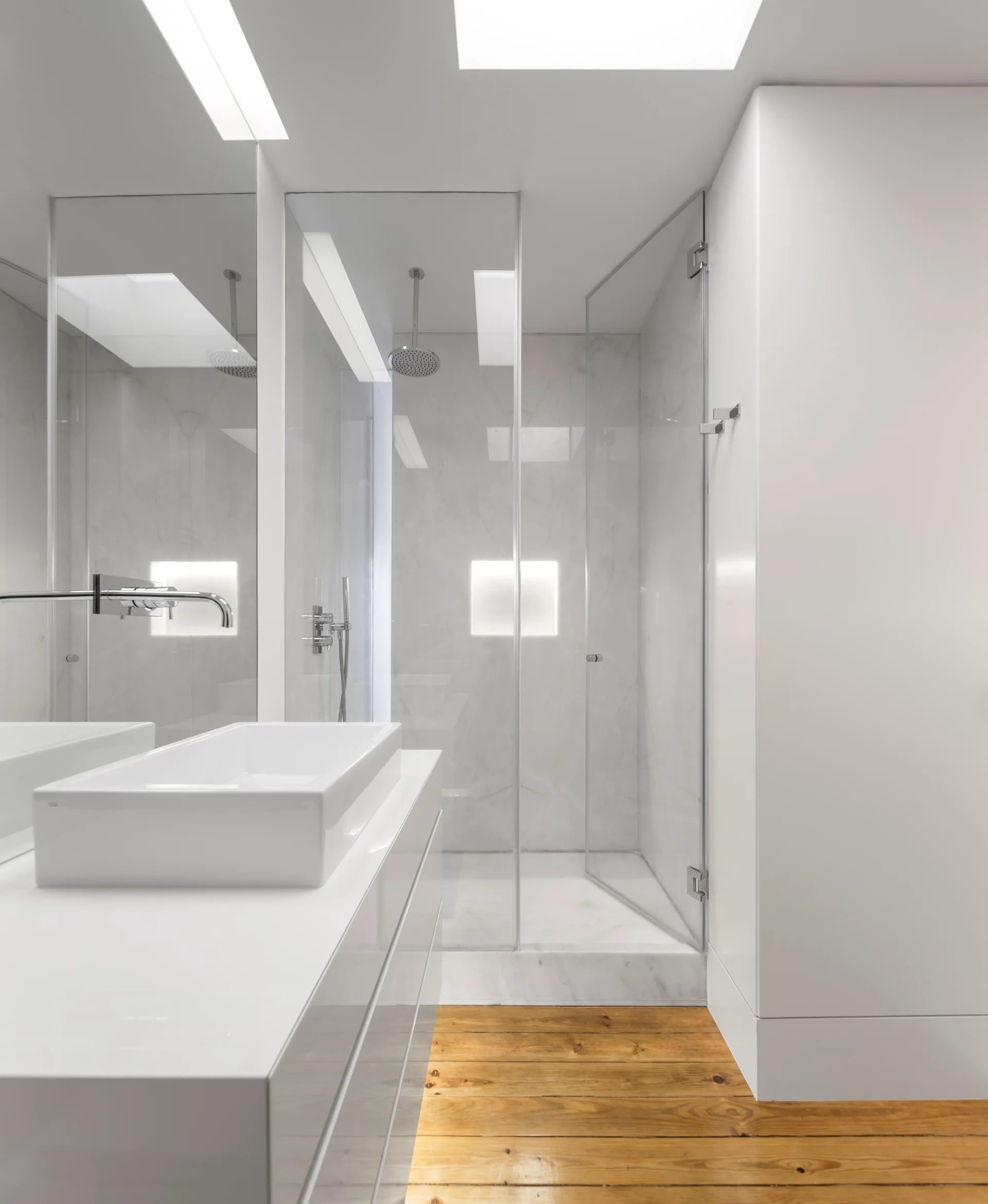 A contemporary white bathroom featuring a glossy vanity with a vessel sink, a glass-enclosed walk-in shower, and natural wood plank floors.