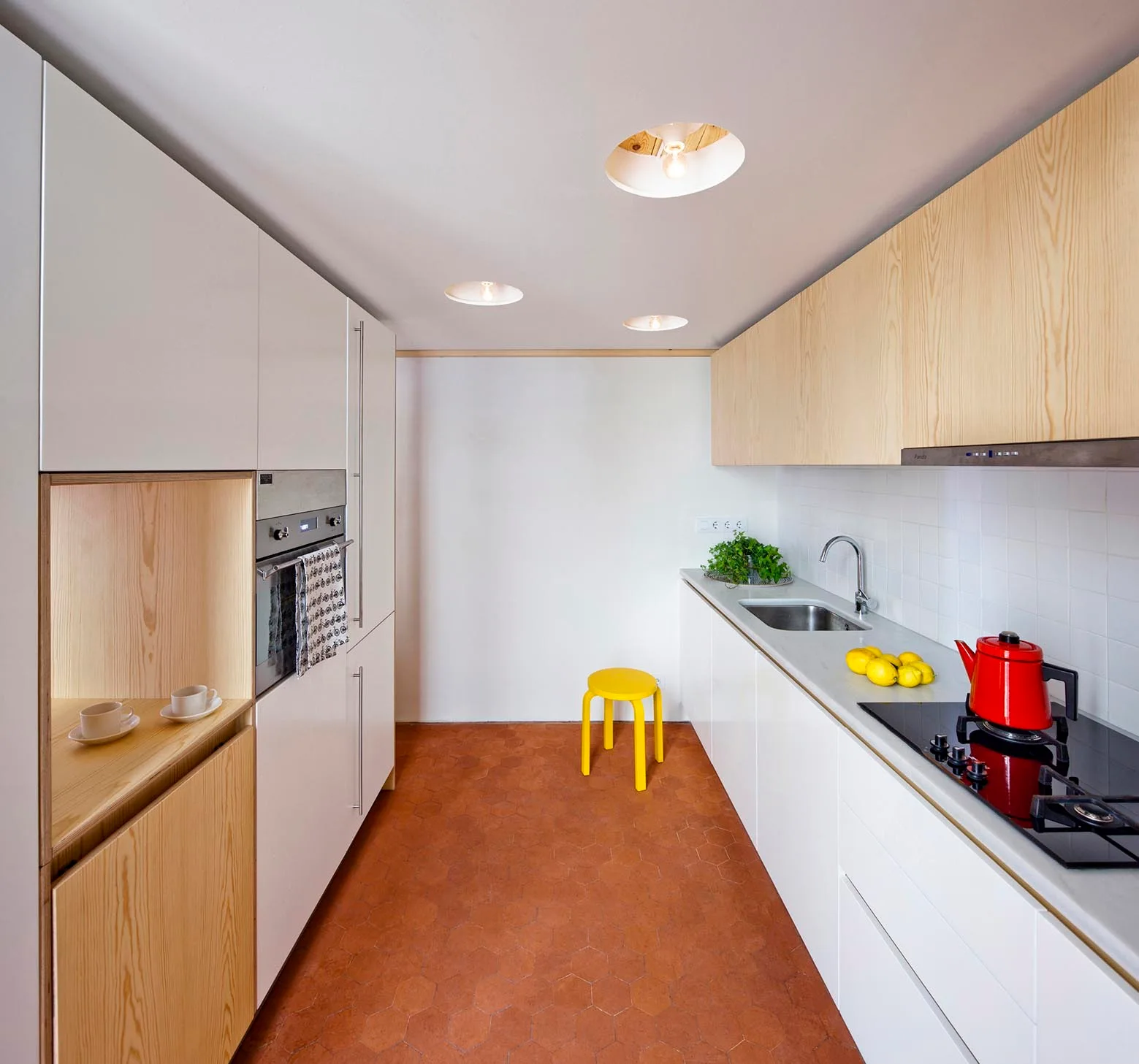 A modern galley kitchen features white and light wood cabinets, a white square tile backsplash, and hexagonal terracotta floor tiles.