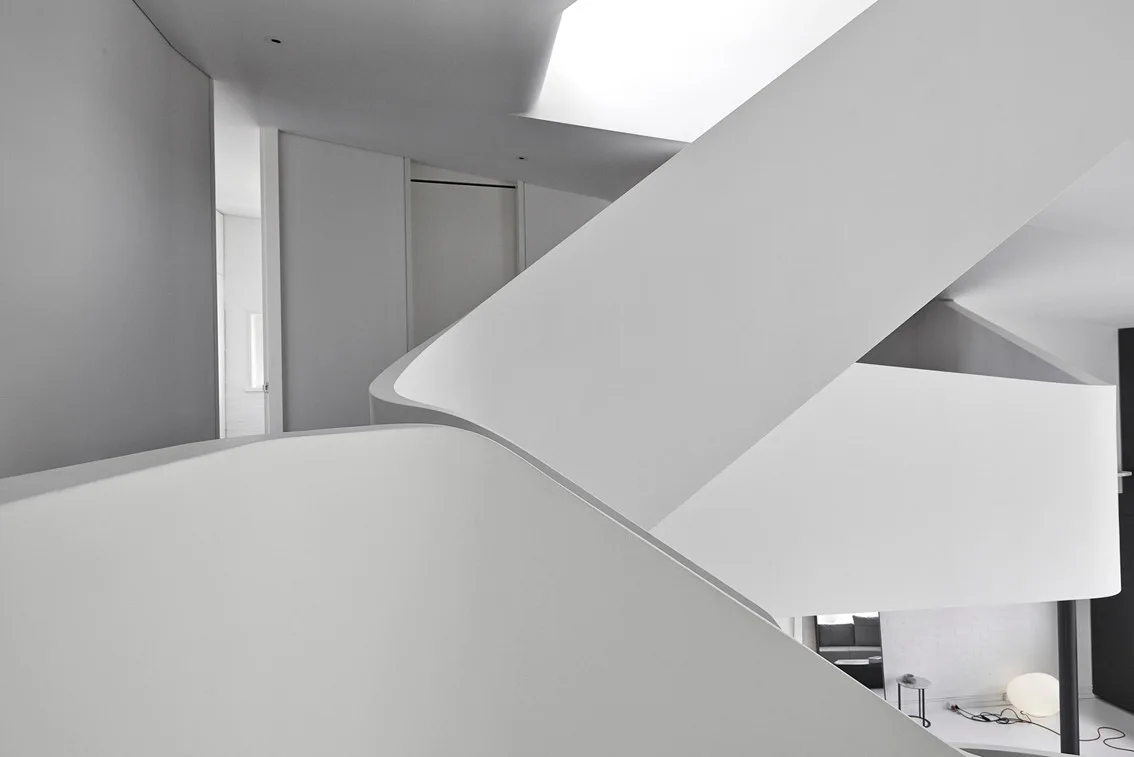 A minimalist architectural interior featuring a large sculptural white staircase with smooth curved handrails and matte white walls.