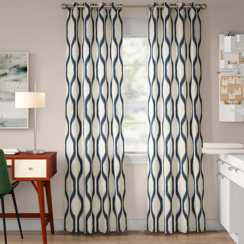 Floor-length navy and beige ikat patterned curtains frame a central window in a home office next to a mid-century desk with a lamp.