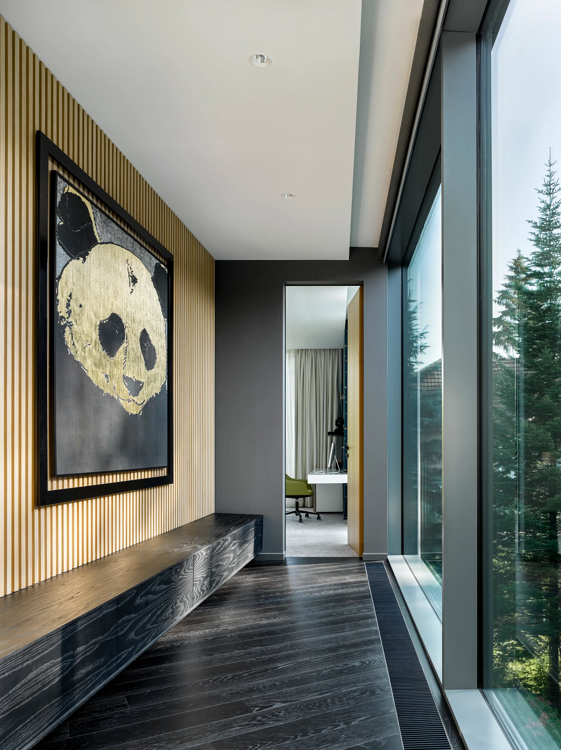 A modern hallway features a vertical wood wall, a large framed panda painting, a low dark cabinet, and floor-to-ceiling windows.