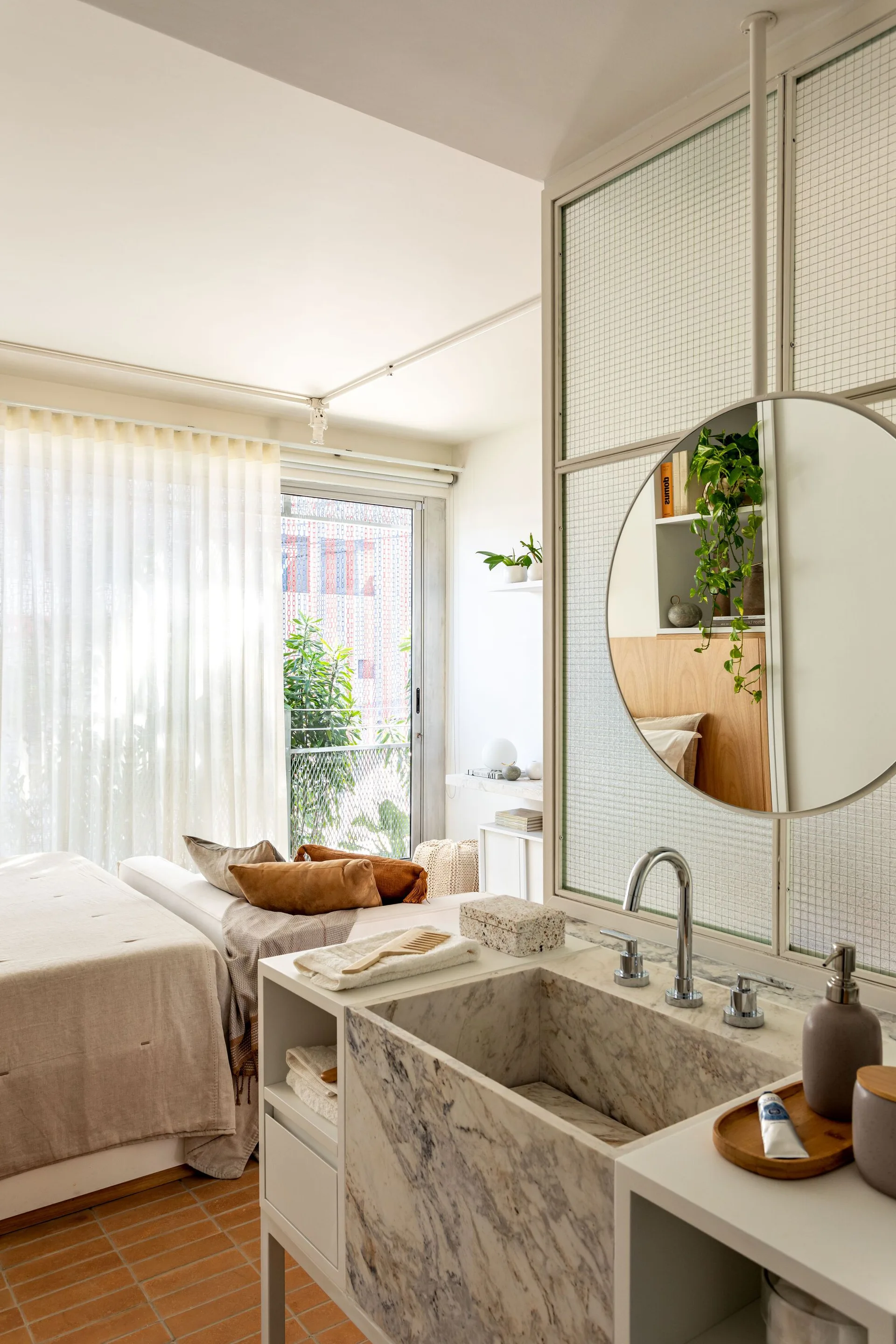 A modern ensuite bedroom features a marble sink vanity in the foreground, separated from the bed area by a textured wire-glass room divider.