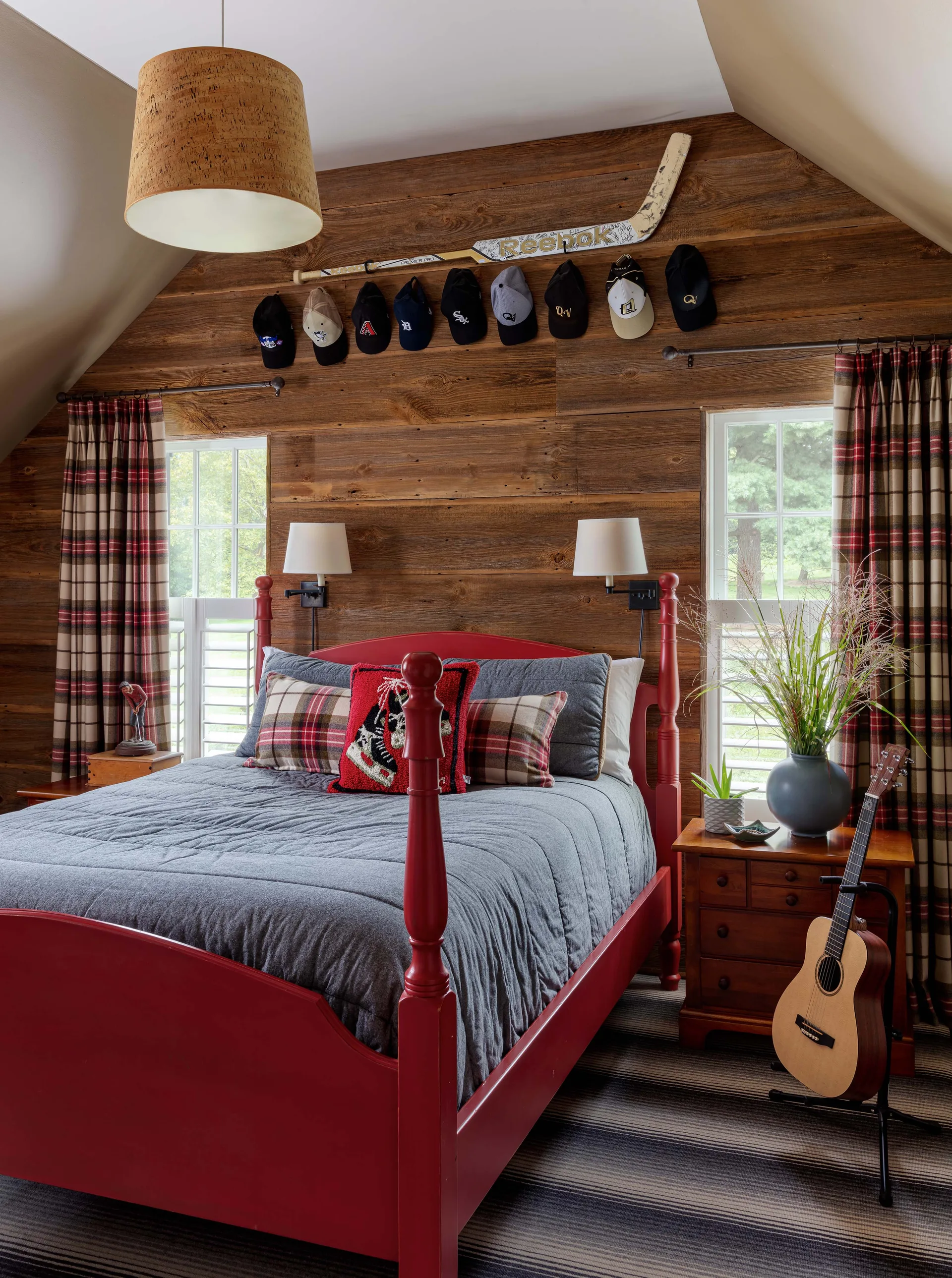 A rustic bedroom features a red wooden poster bed against a wood-planked wall decorated with a hockey stick and baseball caps.
